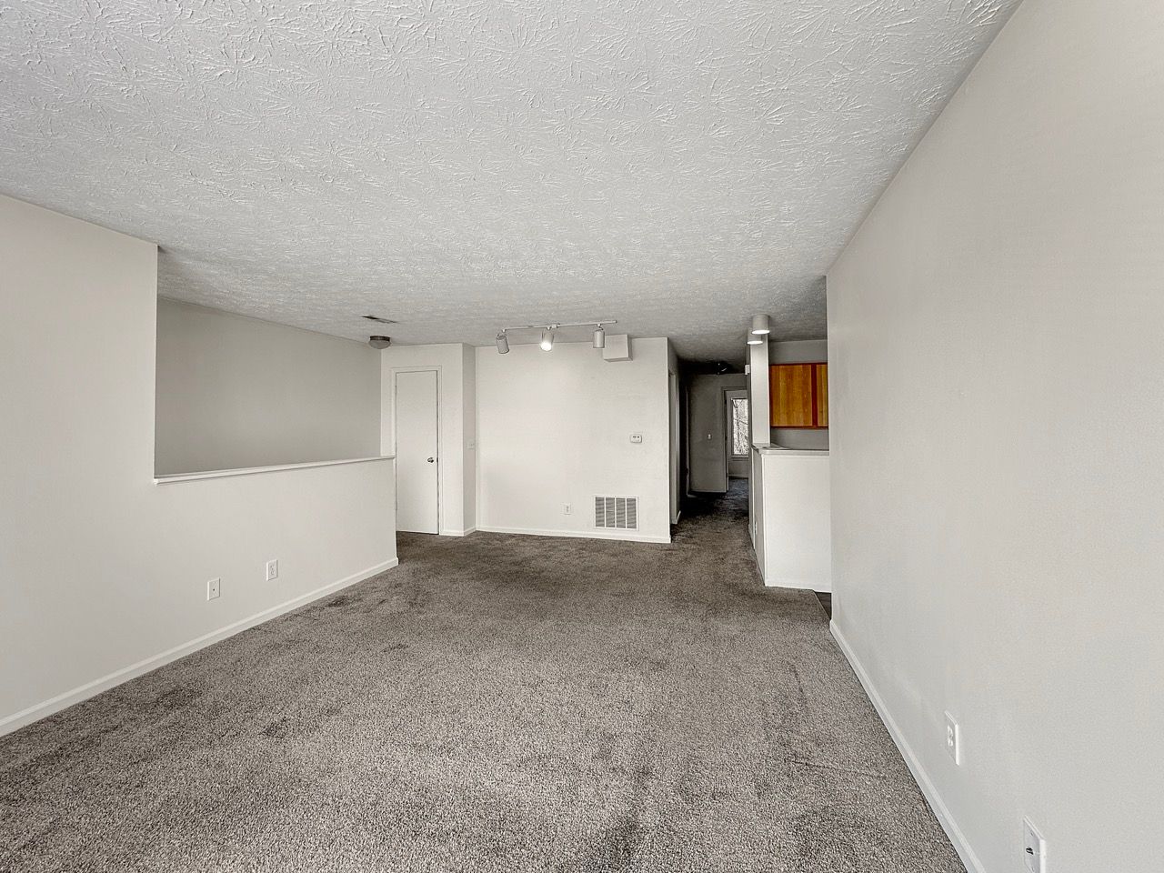 An empty living room with a carpeted floor and white walls.