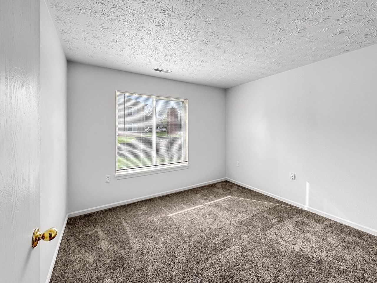 An empty bedroom with a window and carpet.