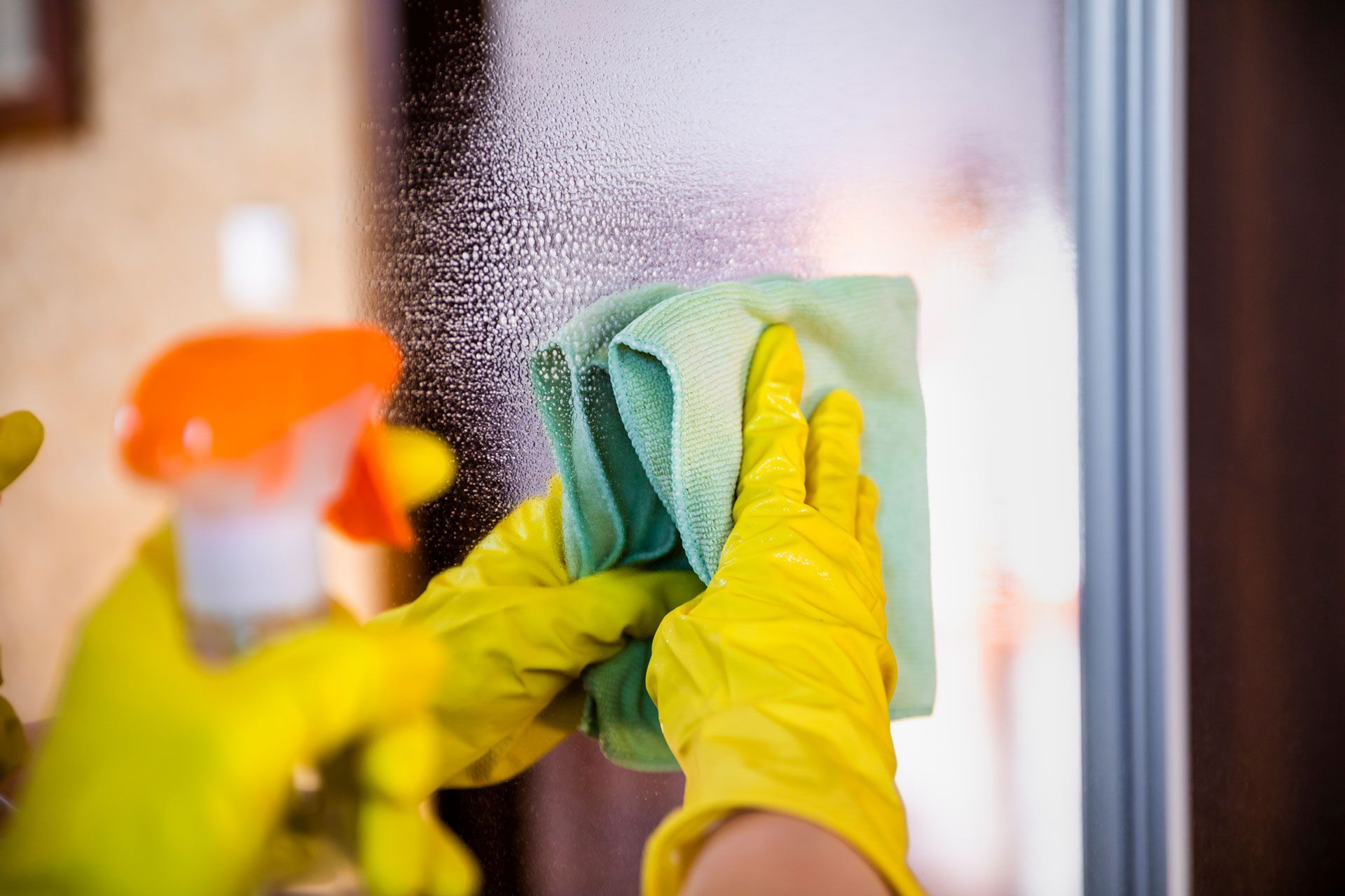 Hands wearing yellow gloves cleaning a glass surface, showcasing professional commercial cleaning