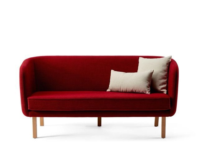 Red upholstered sofa with wooden legs and two light pillows on a white background