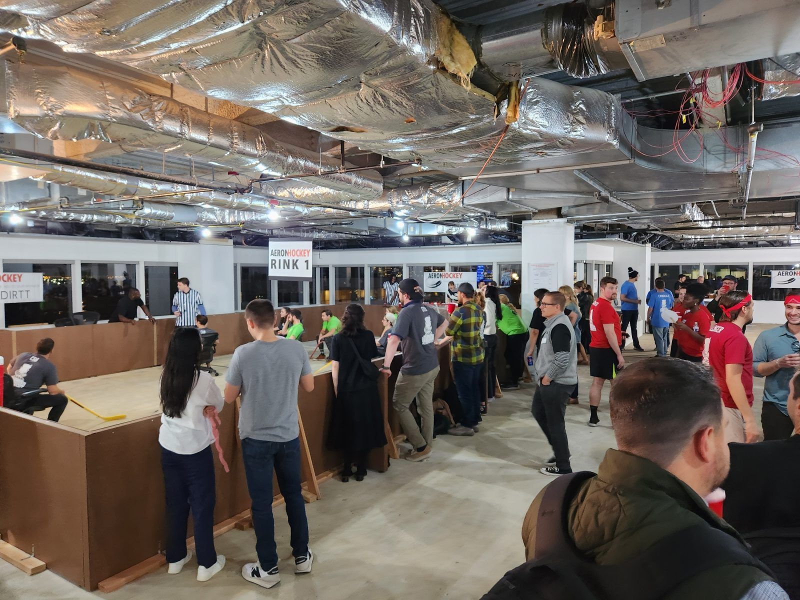 People standing in line at a crowded indoor event with a bare ceiling and check-in counters.