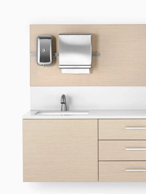 Light wood bathroom vanity with sink, mirror, paper towel dispenser, and tall cabinet on the right