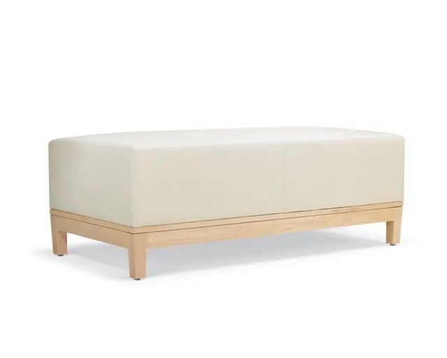 Cream upholstered bench with light wood base and tapered legs on a white background