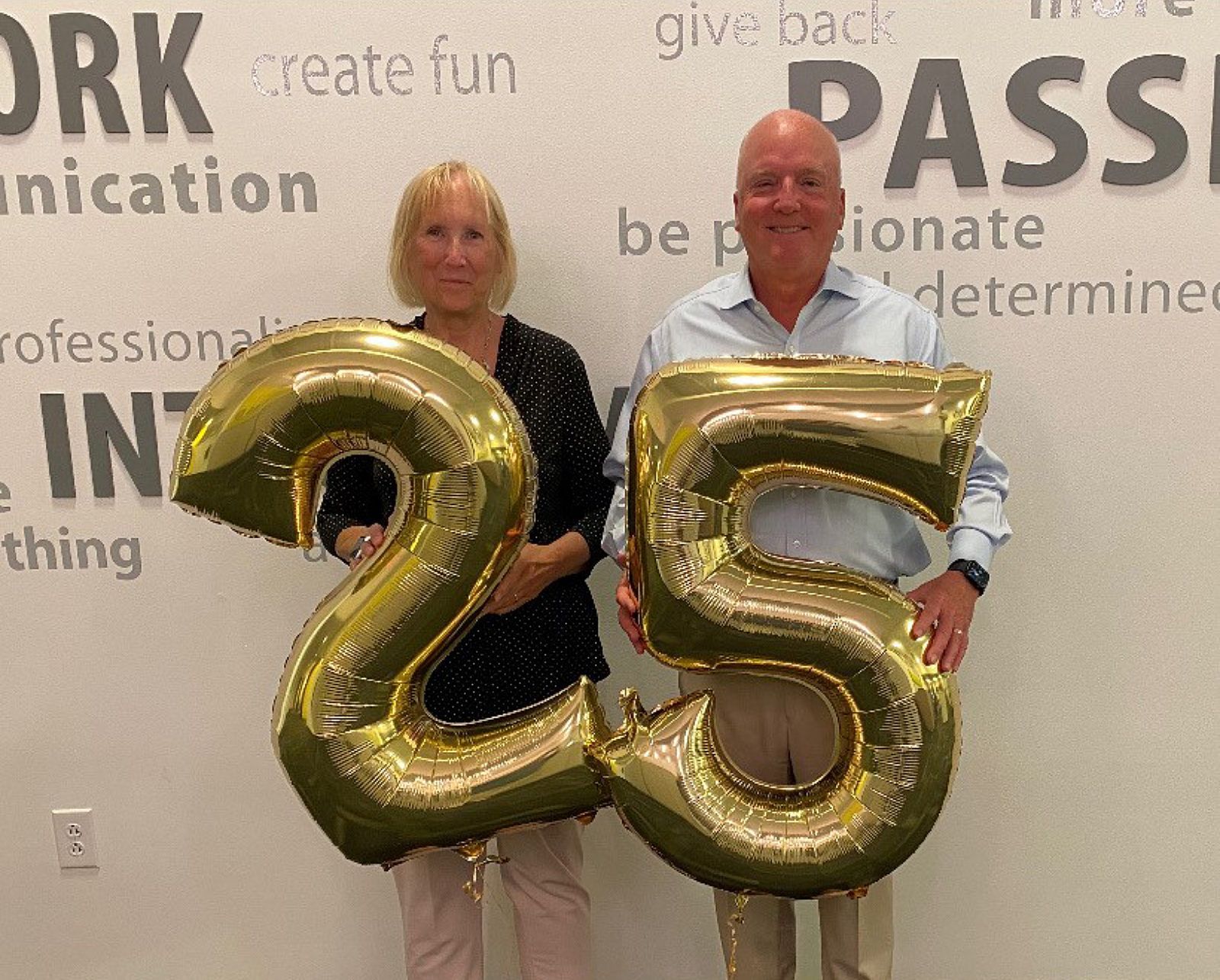 Two people standing behind large gold balloon numbers