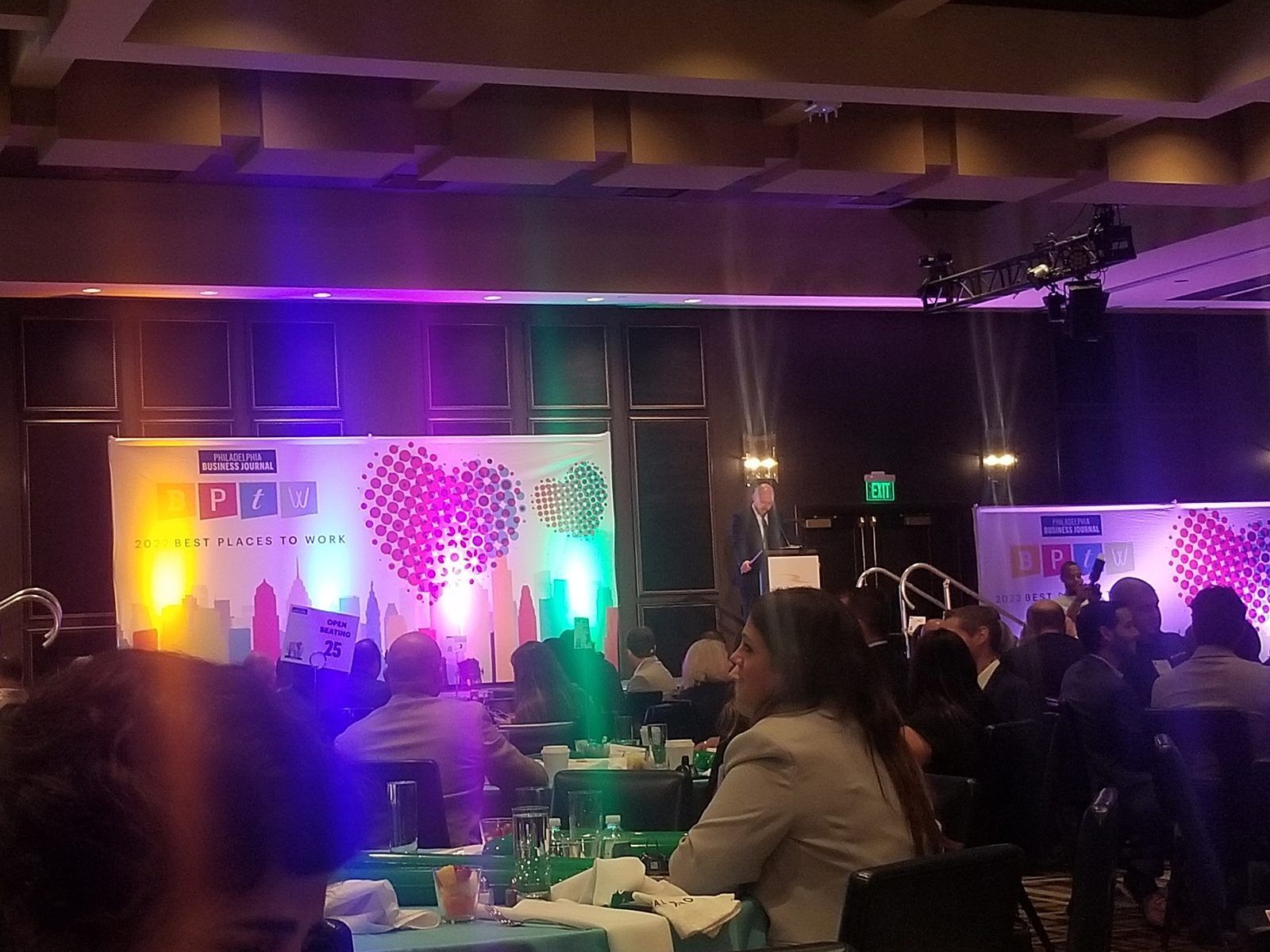 Conference audience watching a brightly lit stage with purple and green lights in a dark venue.