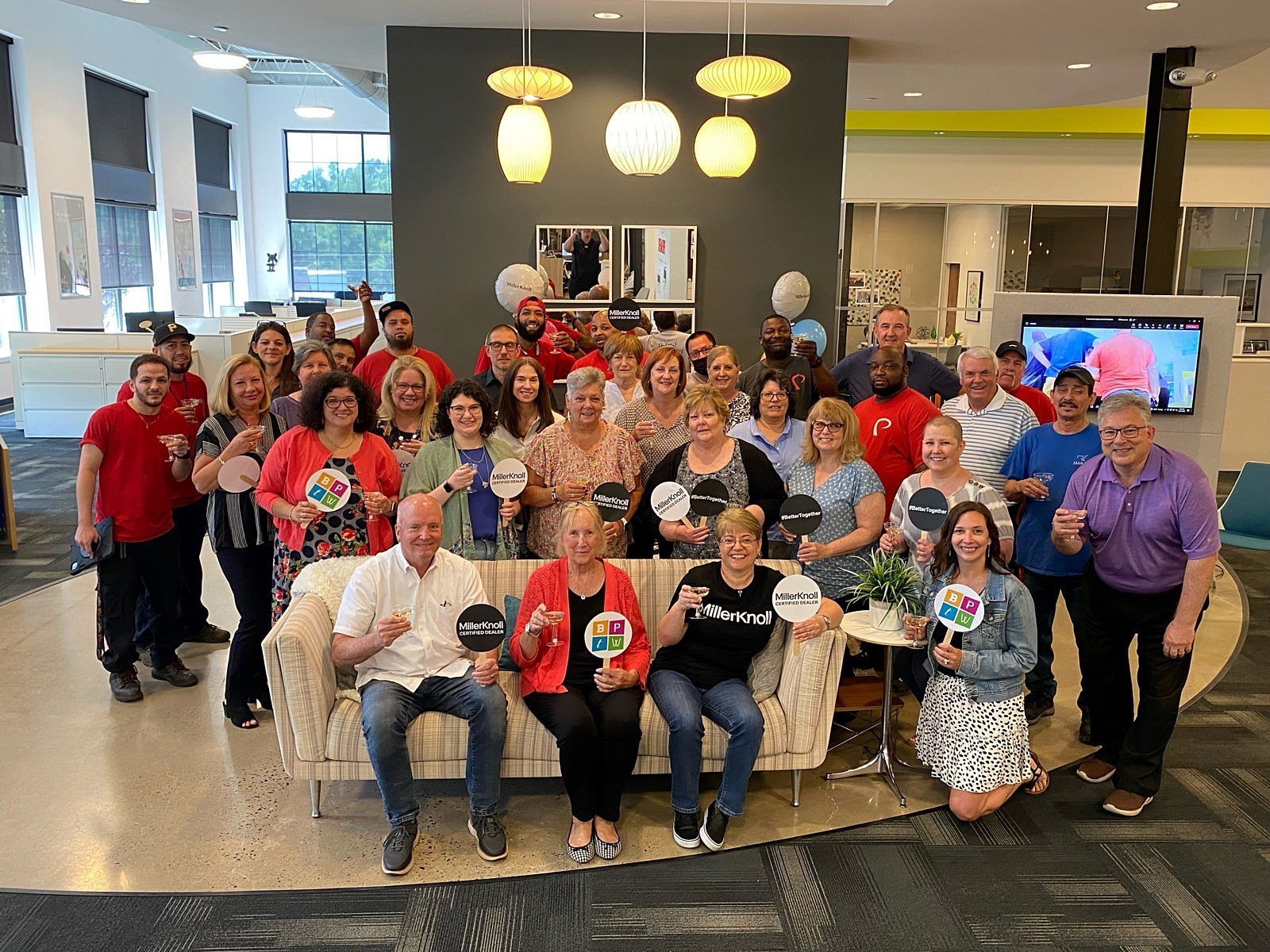 Large group posing in a bright lobby, many wearing red shirts and holding awards or certificates