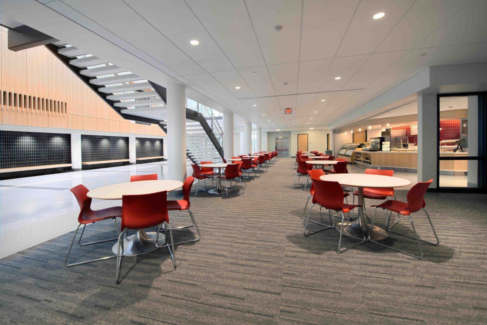 Modern office lounge with red chairs, white tables, and a carpeted open seating area