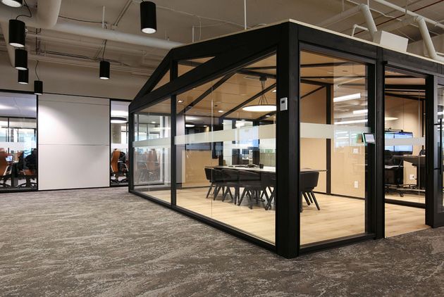 Modern glass conference booth in an open office, with black frame and chairs inside.