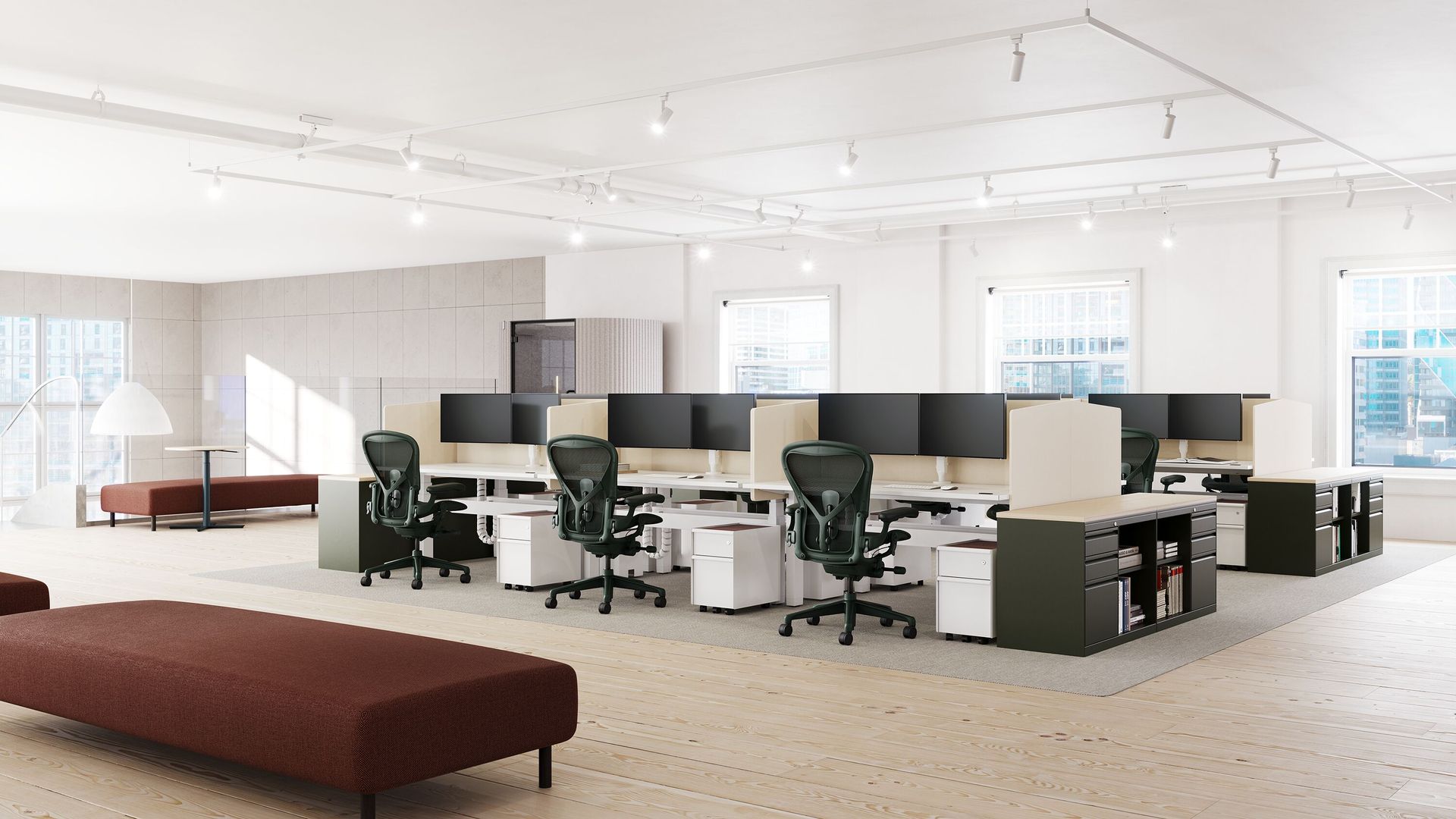 Modern open-plan office with rows of desks, black chairs, large monitors, and white walls in bright daylight