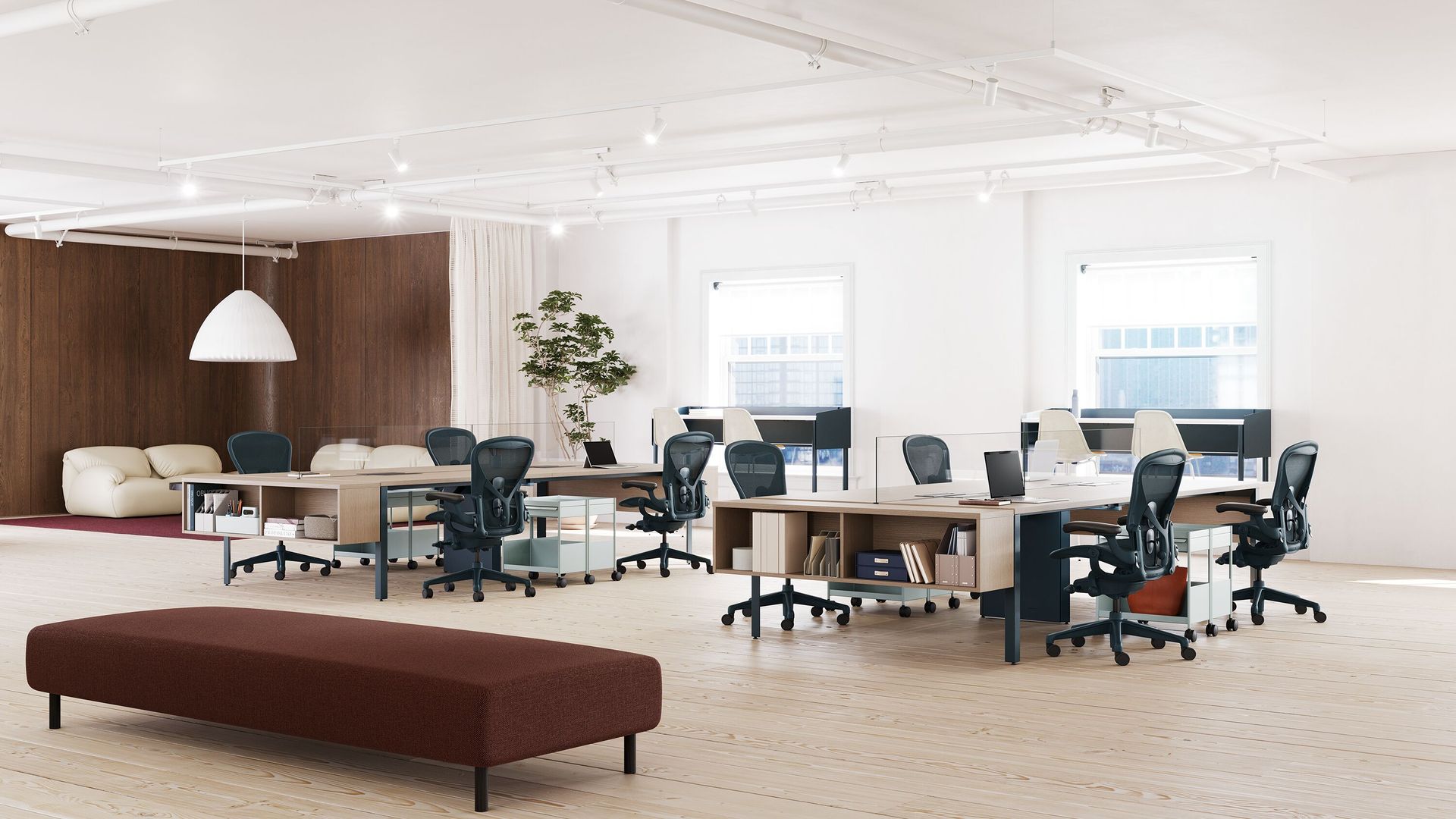 Bright open office with desks, swivel chairs, computers, and a long brown bench in the foreground