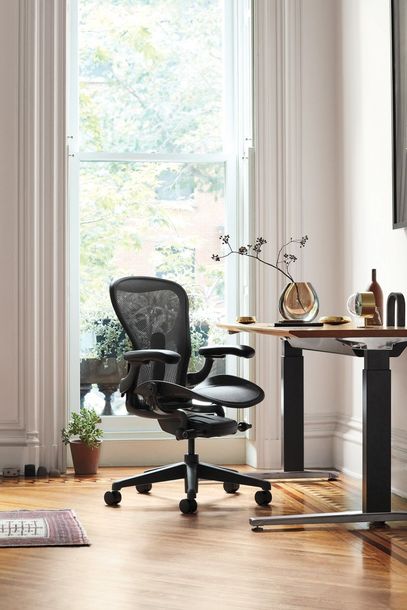 Home office with black ergonomic chair, wooden desk, and large bright window.