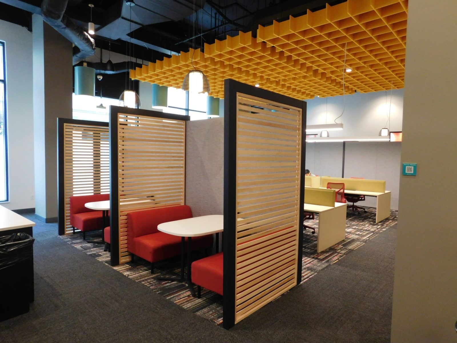 Modern office with red booth seating, wood dividers, and a yellow acoustic ceiling