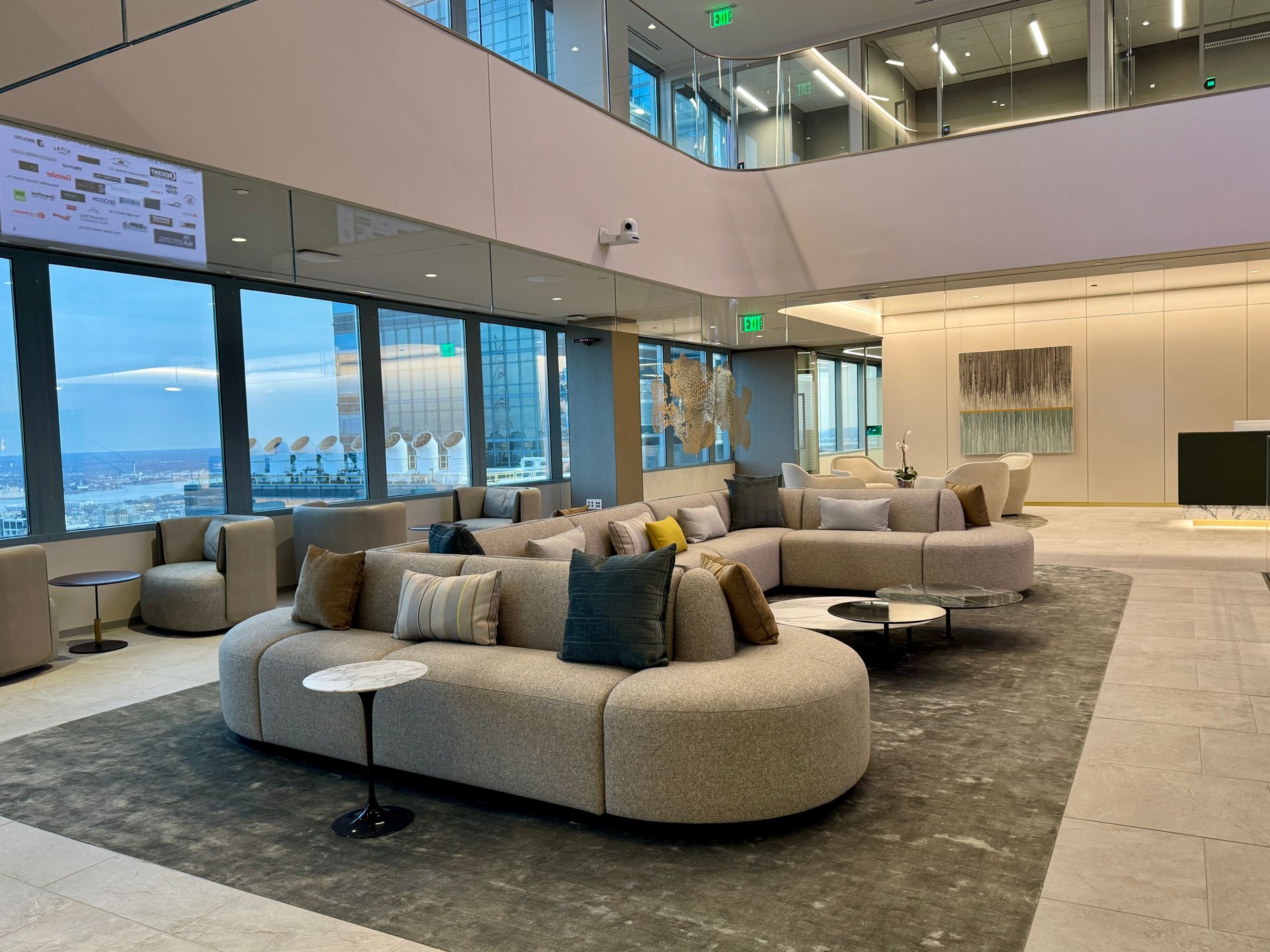 Modern lobby with curved beige sofas, large windows, and a high ceiling overlooking a city view