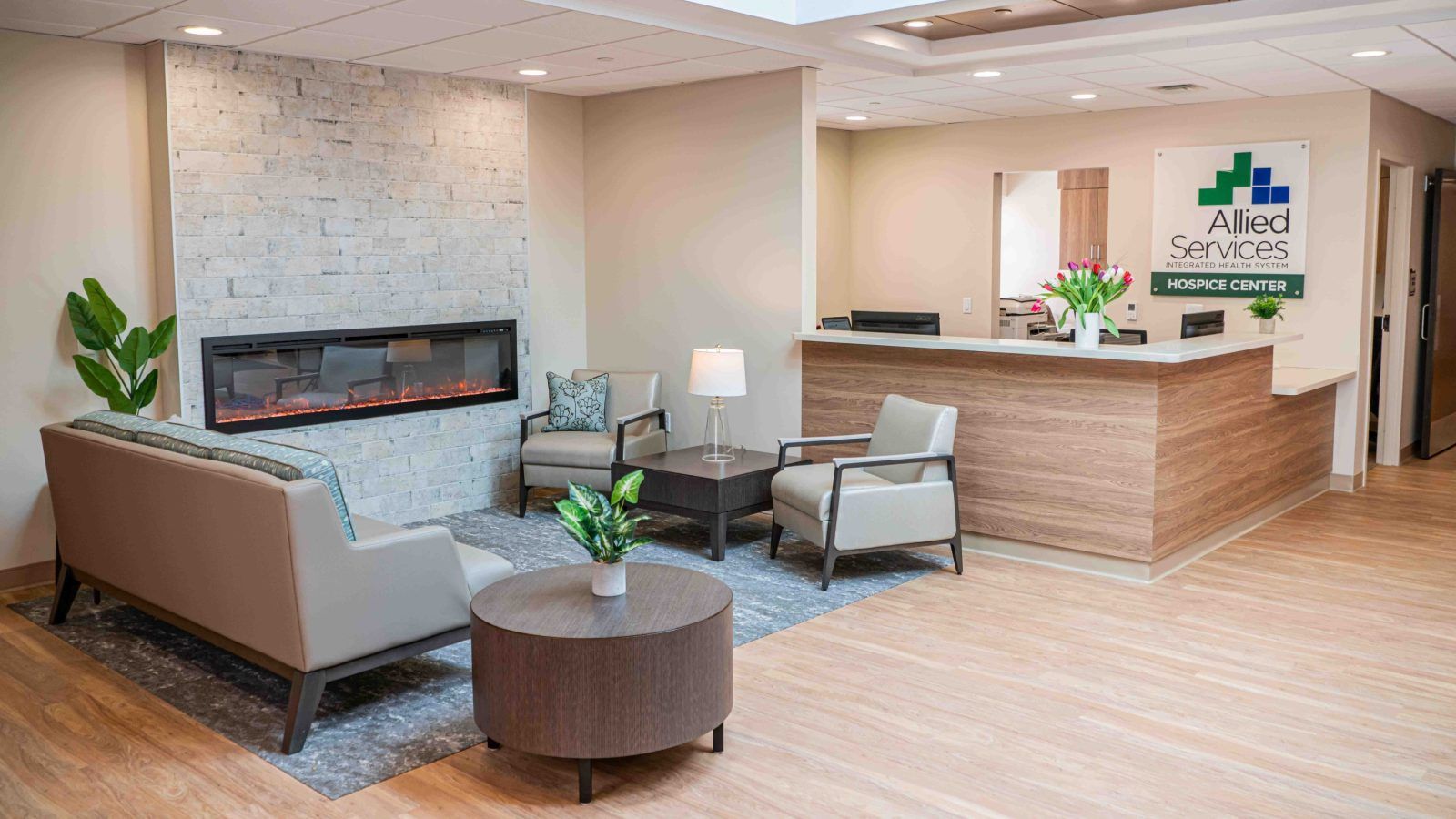 Bright hotel lobby with fireplace seating and a front desk, in beige and wood tones