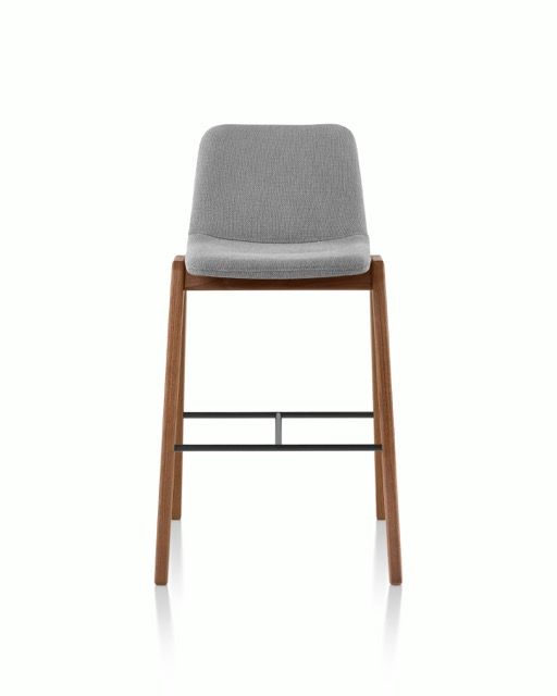 Gray upholstered bar stool with wooden legs and a metal footrest on a white background