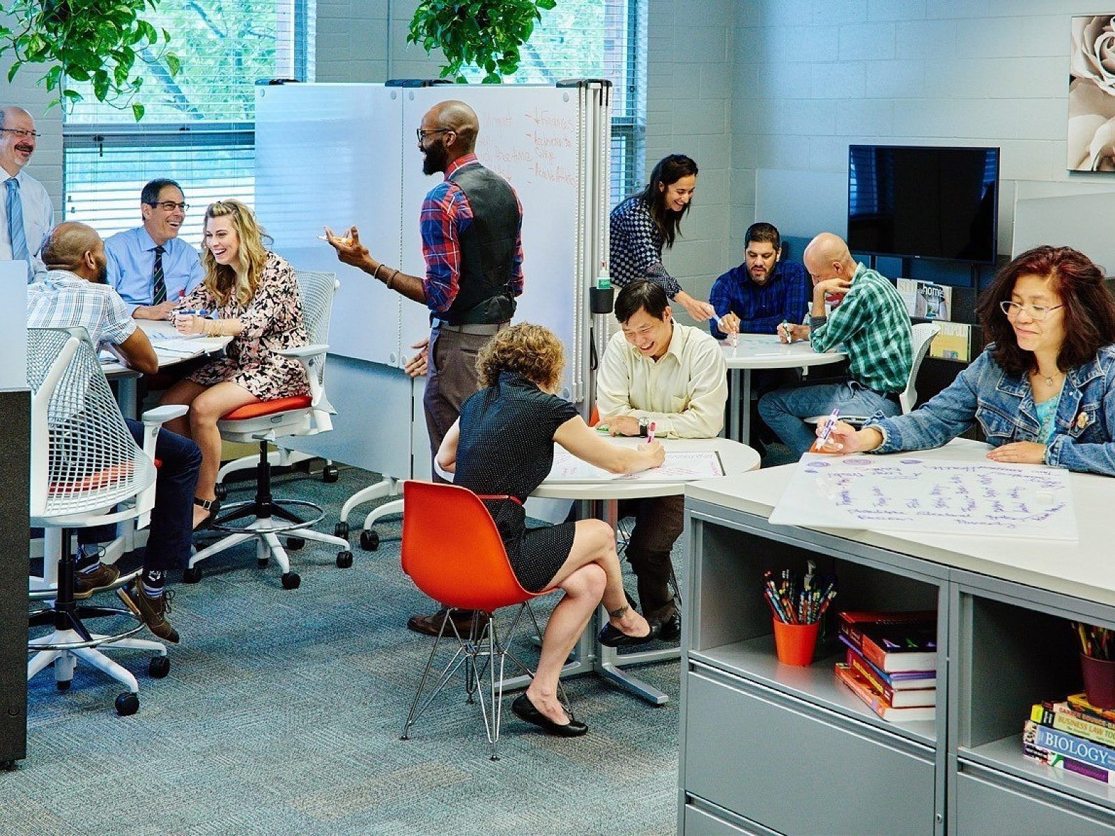 People meeting and working in a bright modern office with desks, chairs, and laptops.