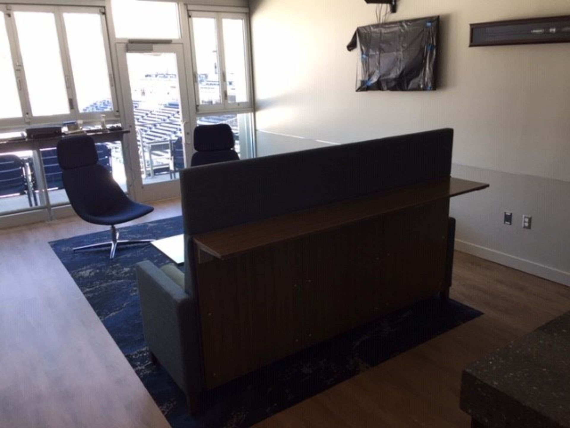 Modern office lounge with chairs, a table, wall-mounted TV, and sunlight through large windows