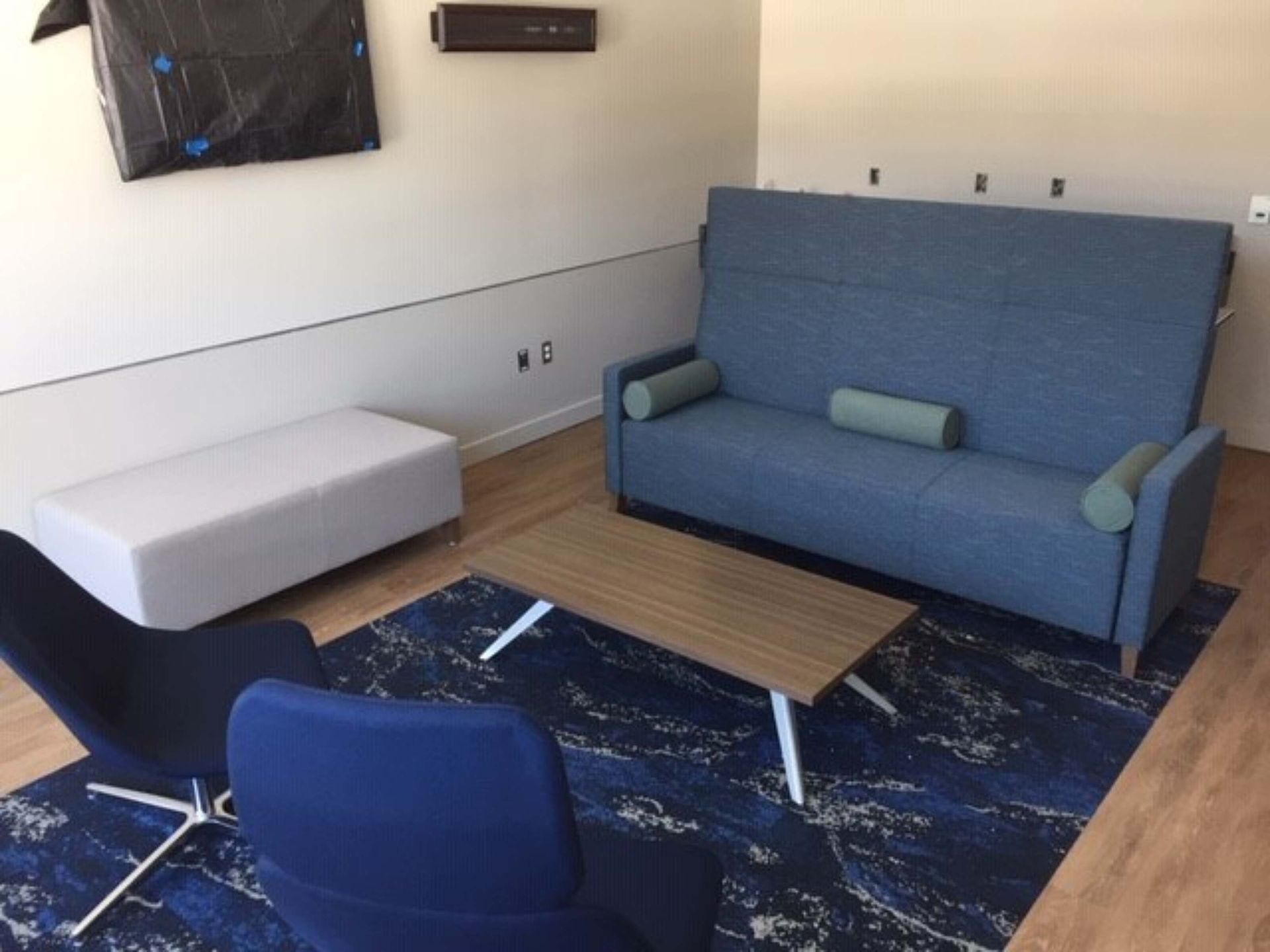 Modern living room with blue sofa, white ottoman, wood coffee table, and blue chair on a patterned rug