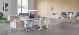 Modern open-plan office with desks, chairs, laptops, and large windows in a bright, minimalist workspace