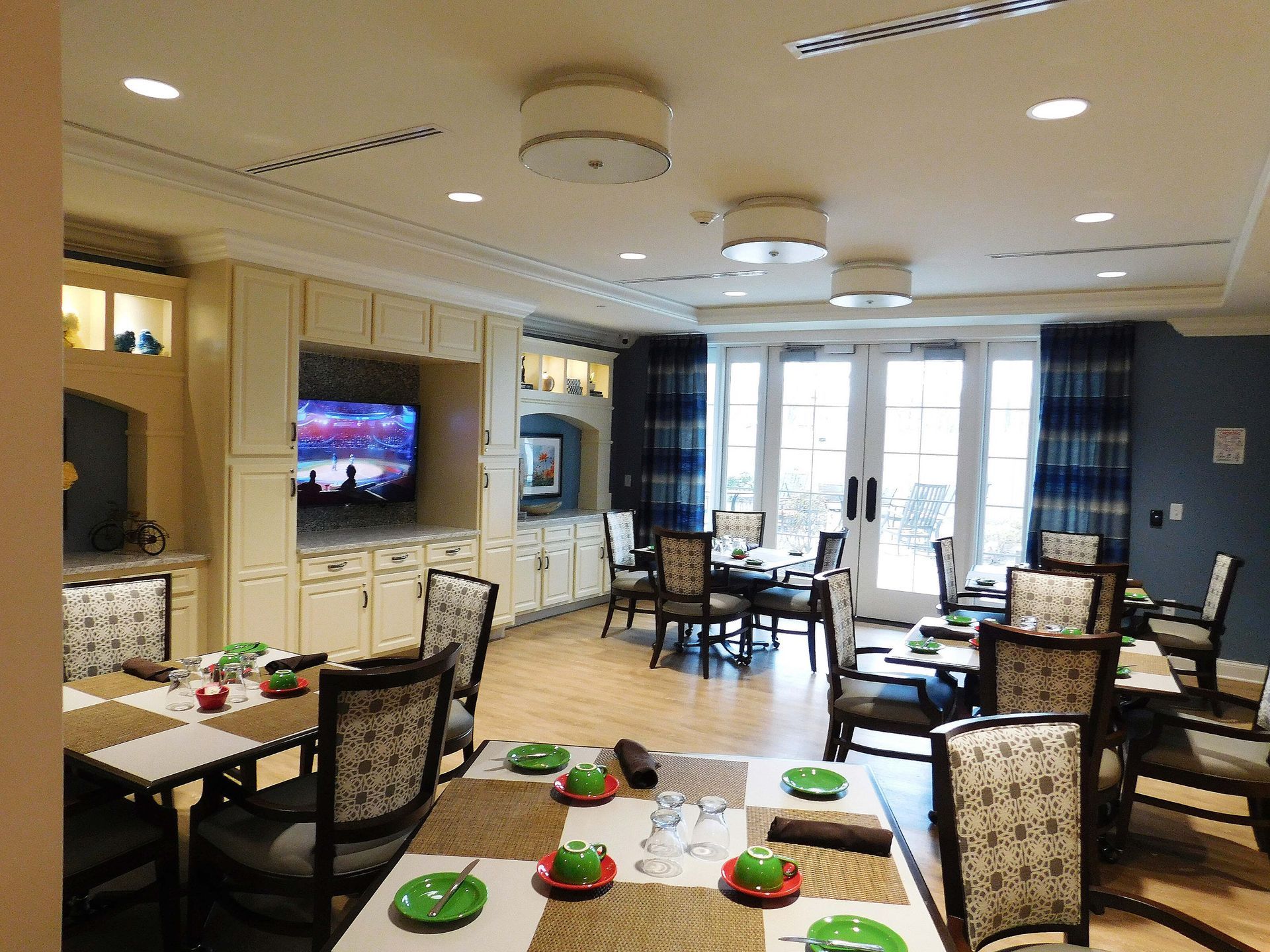 Bright dining room with tables, chairs, wall-mounted TVs, and large windows in a modern lounge.