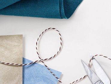 Gift wrapping supplies with blue and silver paper and striped twine on a white background
