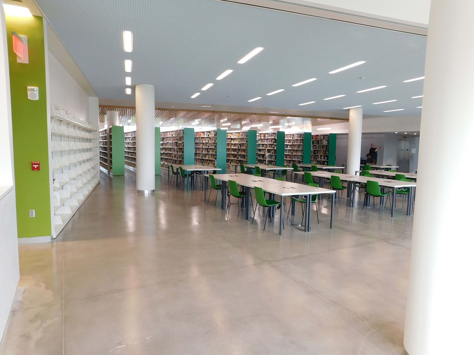 Modern library study area with long tables, green chairs, and bright ceiling lights