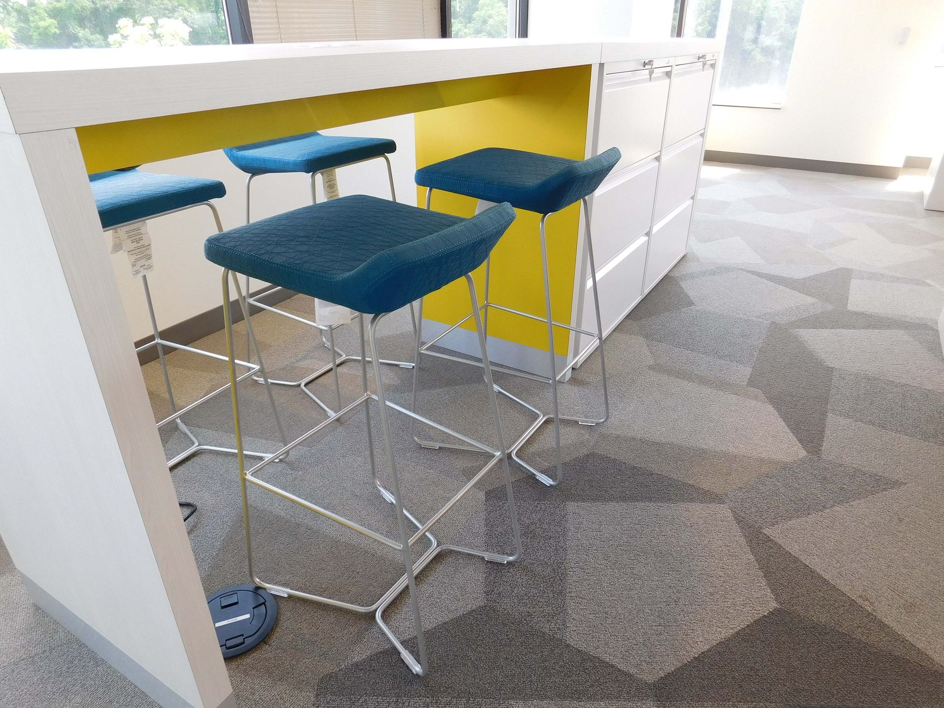 White counter with blue stools in a bright office lounge area on a gray patterned carpet