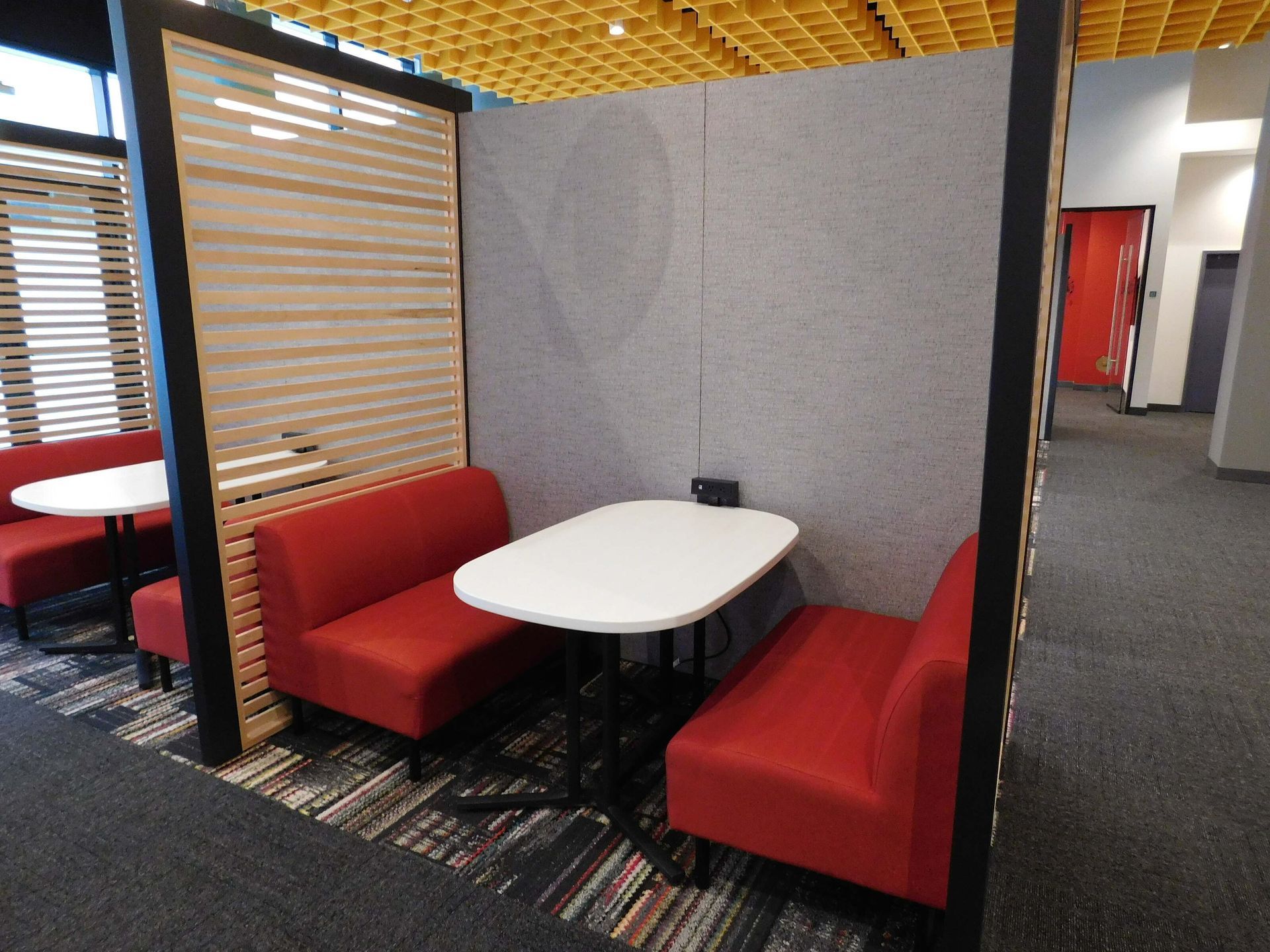 Small booth seating area with red benches, white table, and gray partition in an office or cafe.