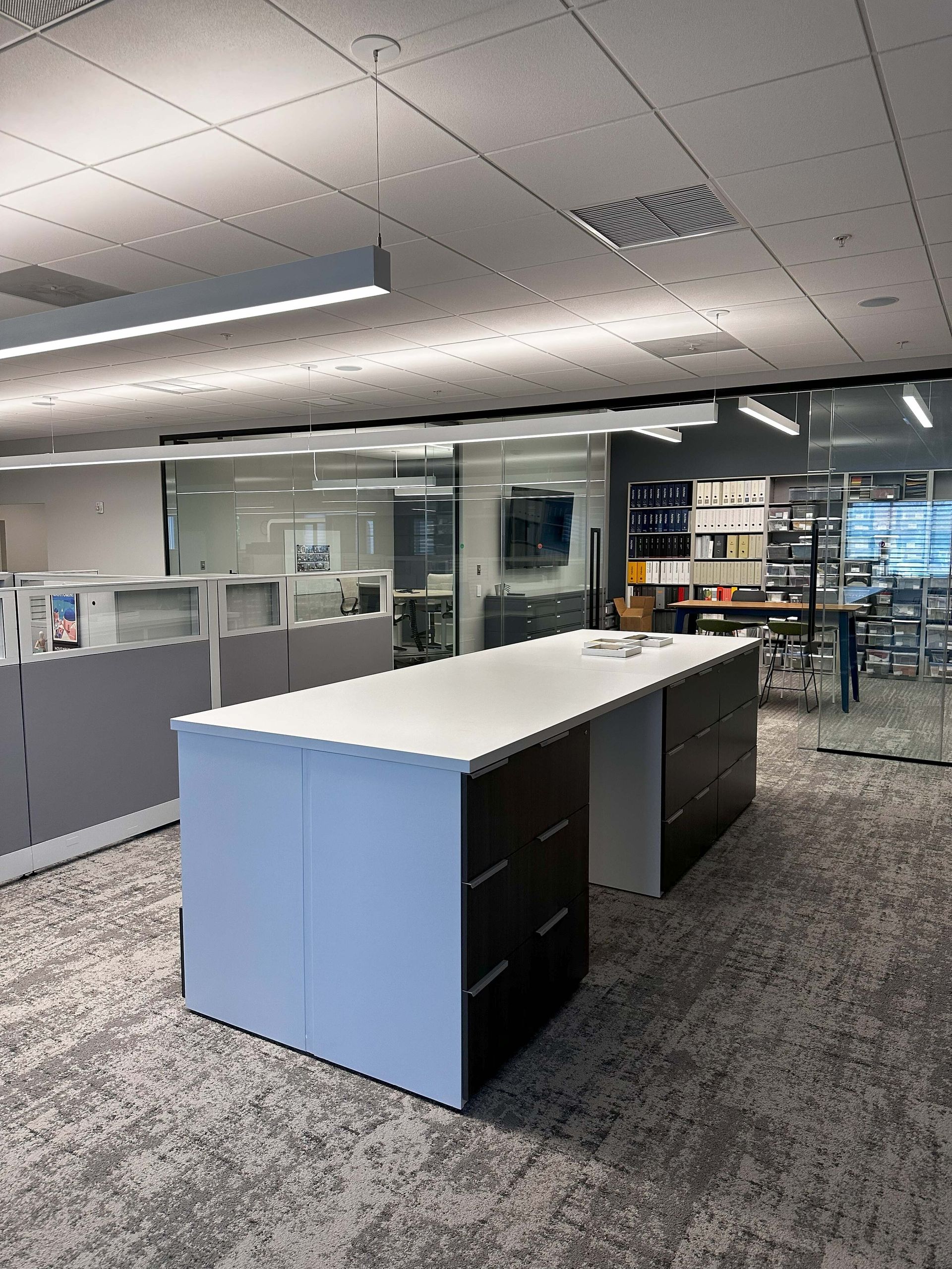 Empty modern office with a white-topped island desk and glass-walled meeting area in the background