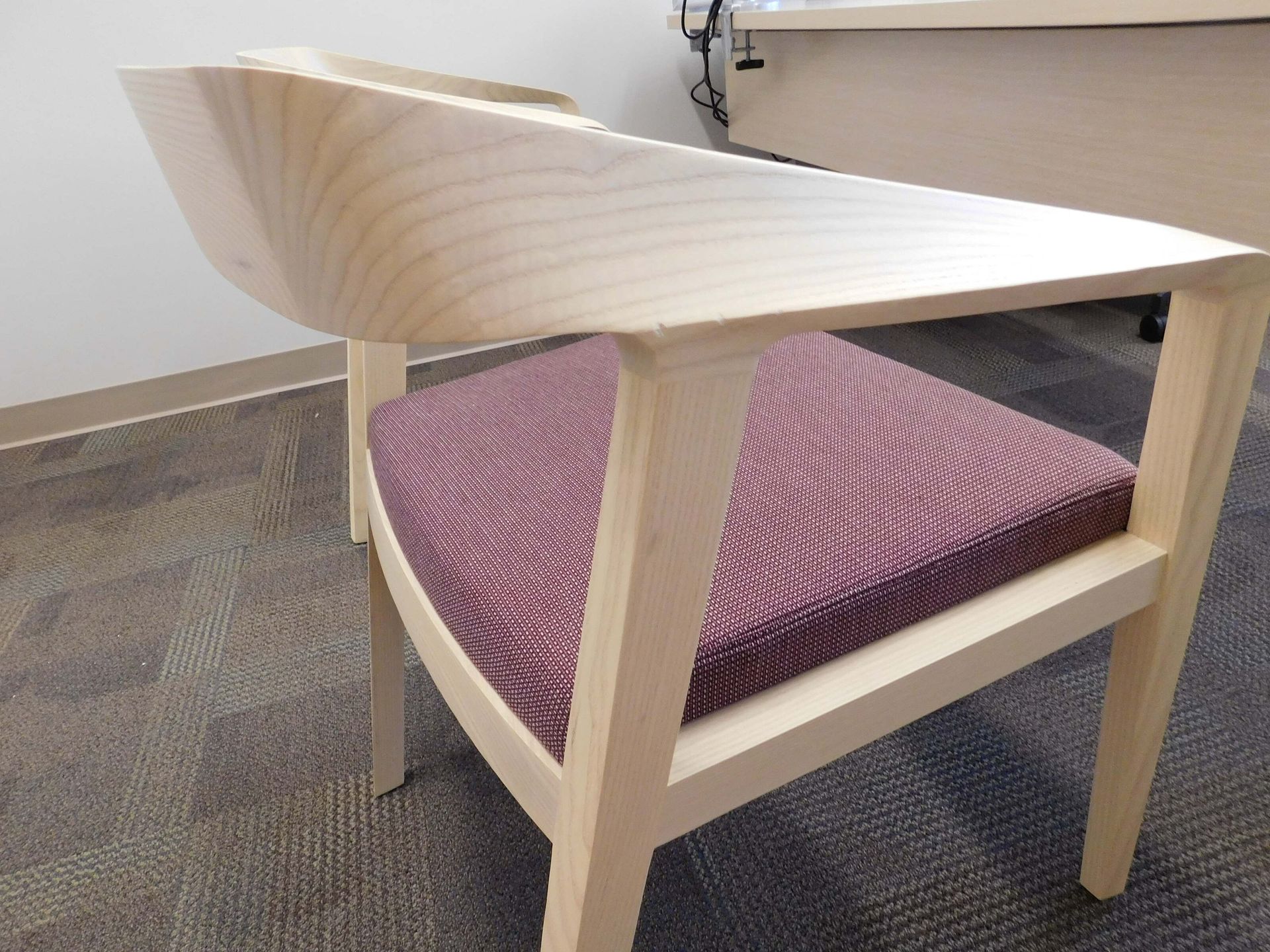 Wooden chair with a curved pale seat and purple cushion on a carpeted floor