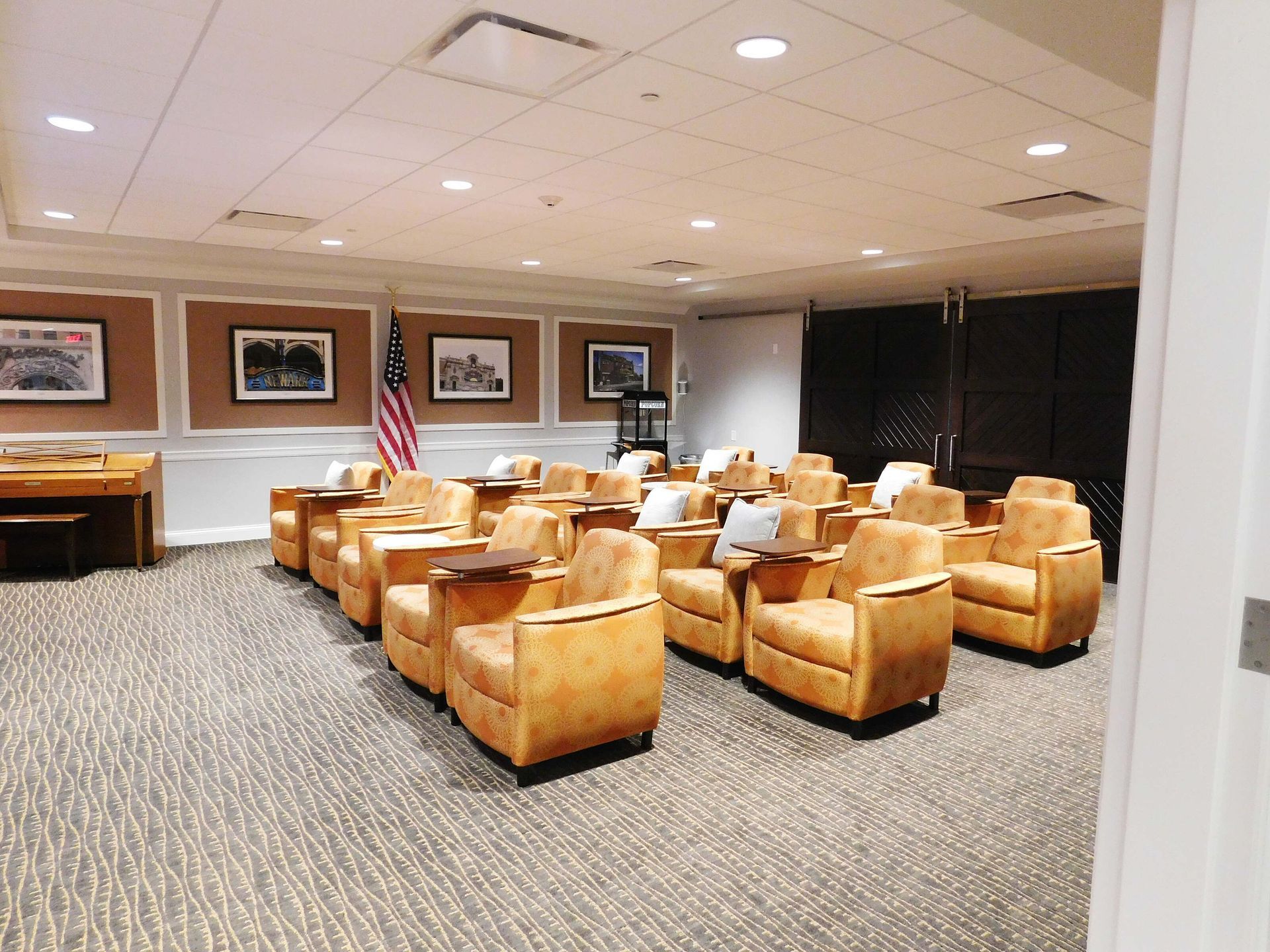 Conference room with tan leather chairs, small tables, and framed wall art on beige carpet.