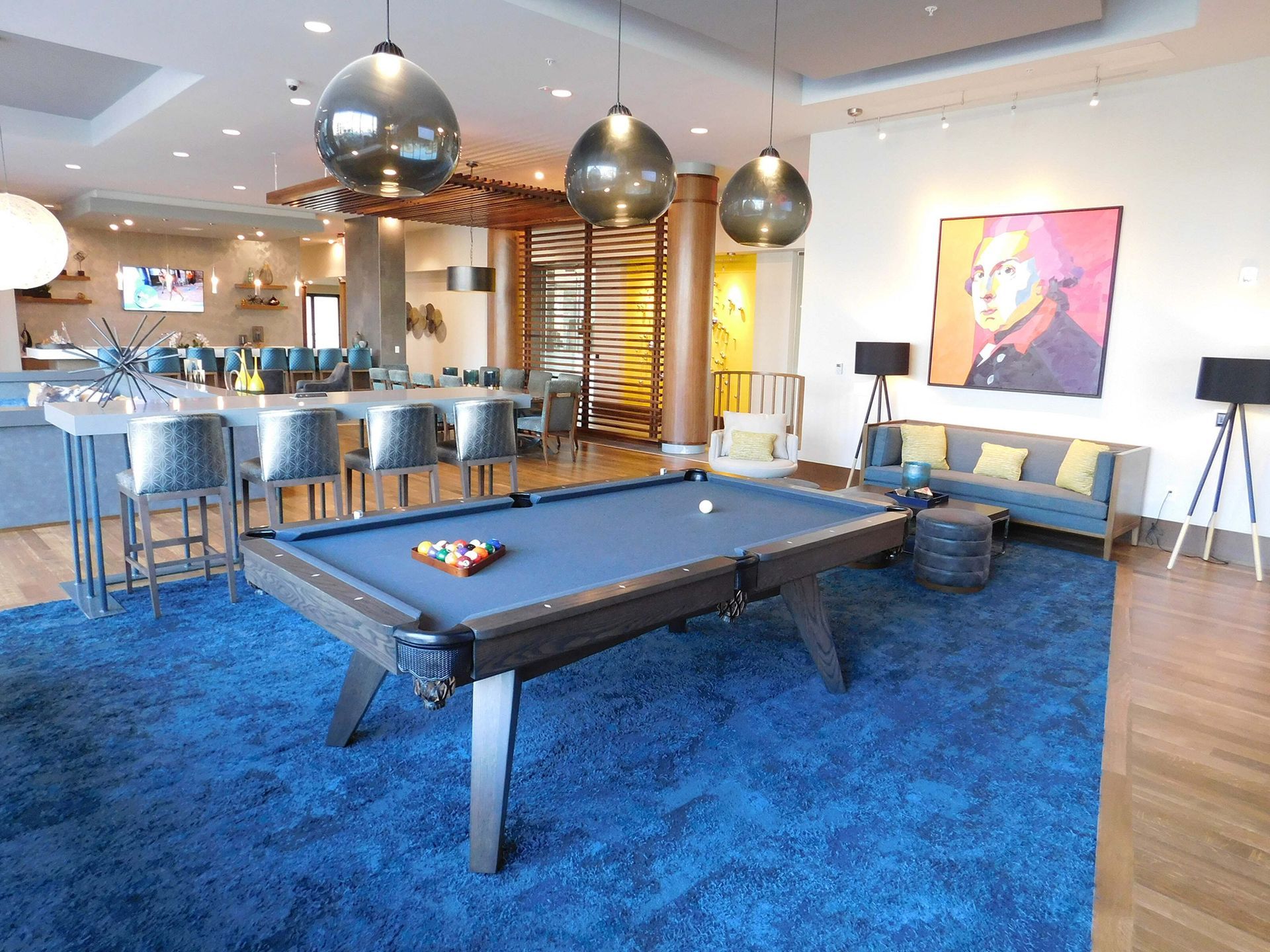 Modern game room with a blue pool table, bar seating, and lounge area under pendant lights