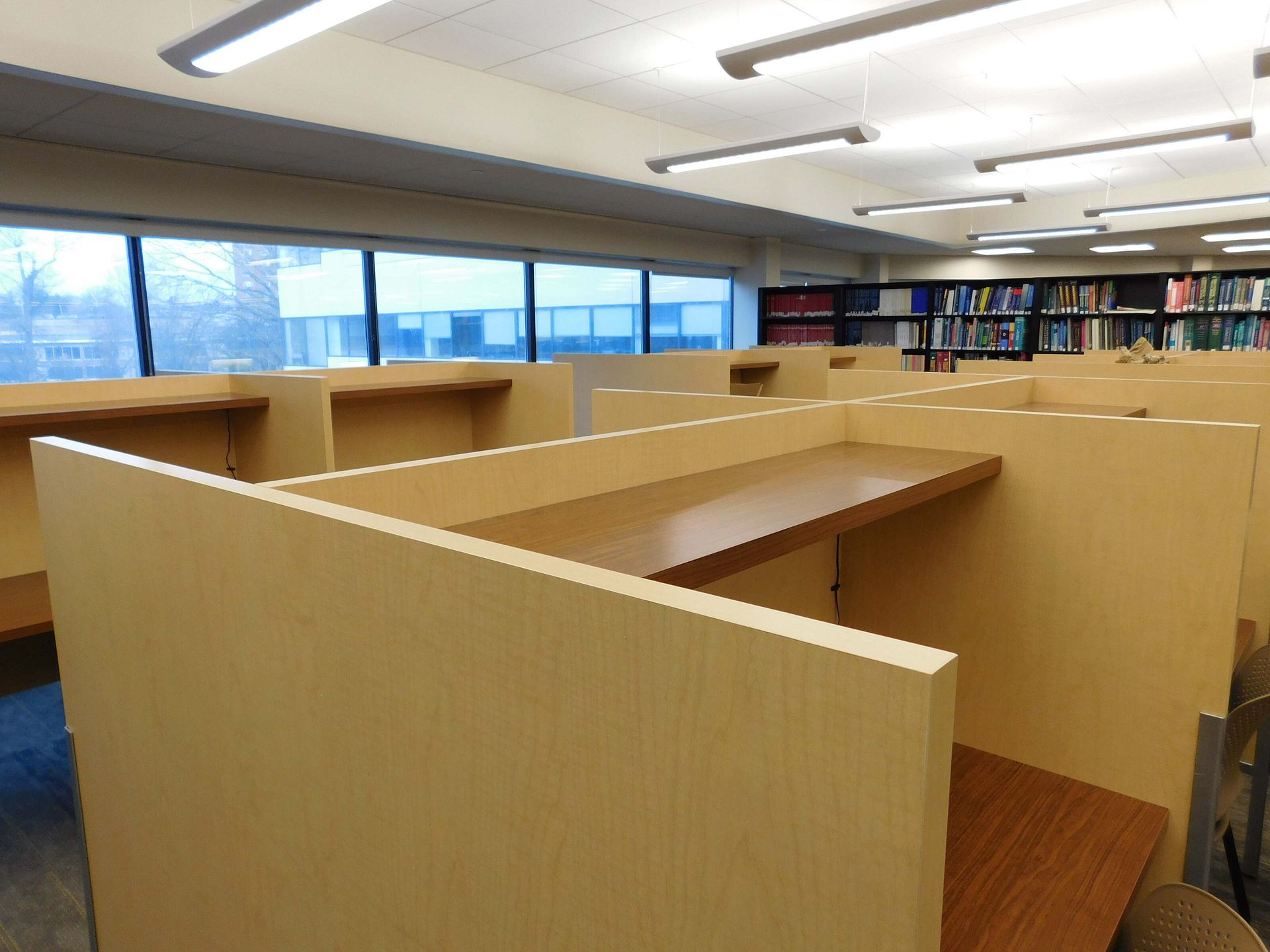 Library study carrels with wooden partitions and shelves under fluorescent lights.