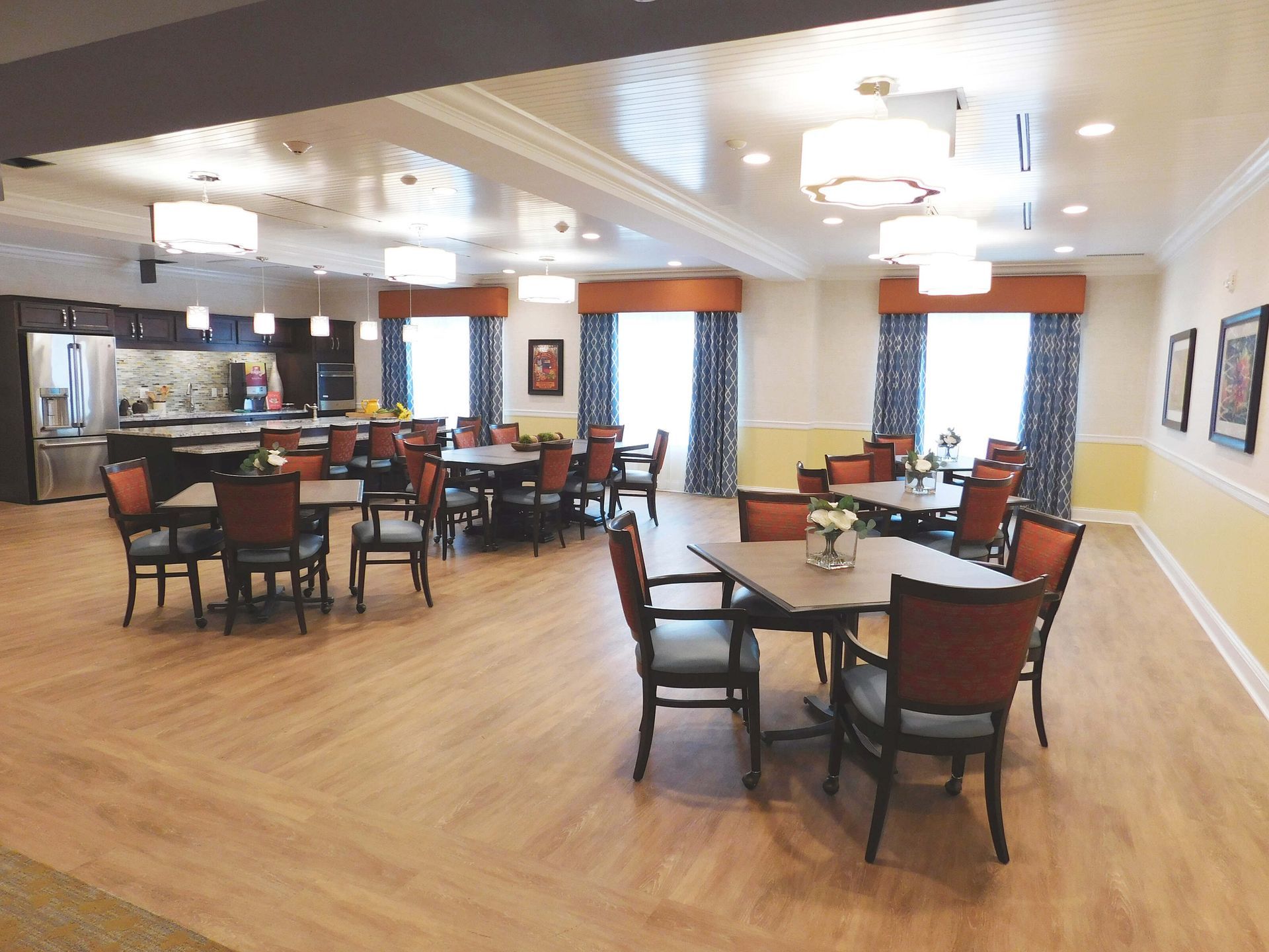 Spacious dining room with round tables, red chairs, wood floors, and bright ceiling lights.