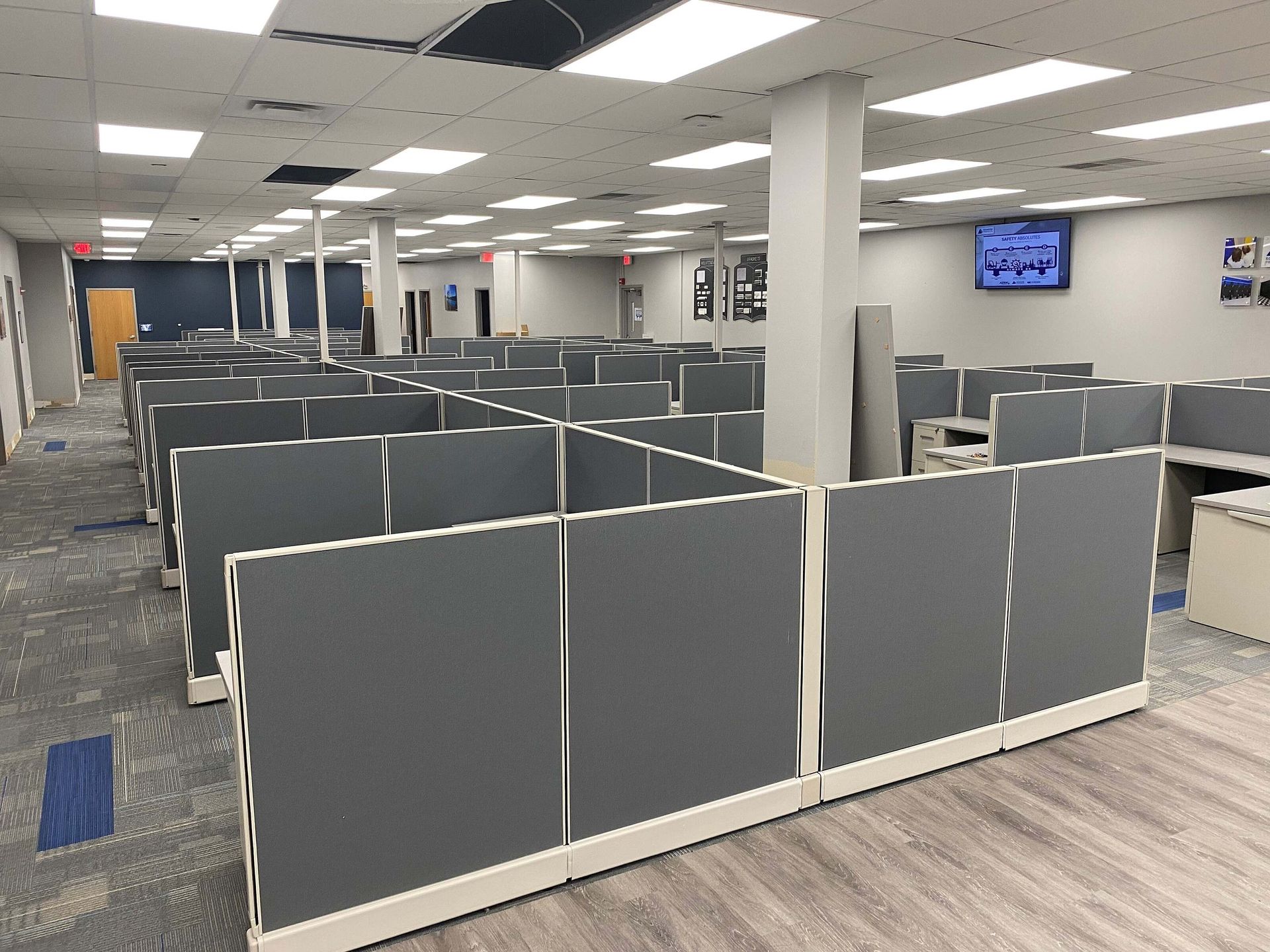 Empty office cubicle workspace with gray partitions, white columns, and overhead fluorescent lighting
