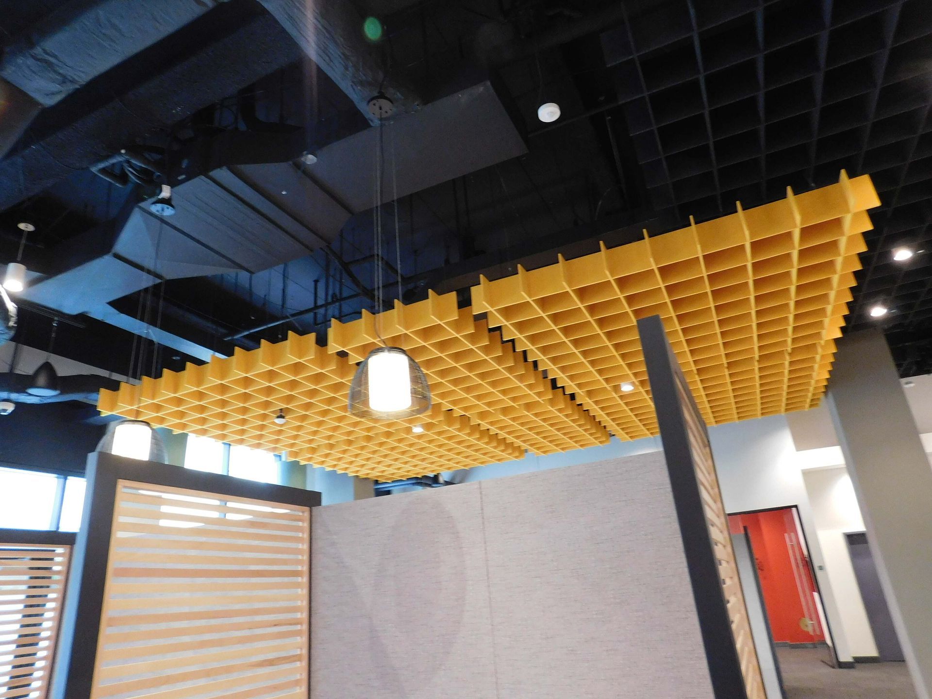 Modern interior with a yellow acoustic ceiling grid and exposed black ceiling beams above white partition walls.