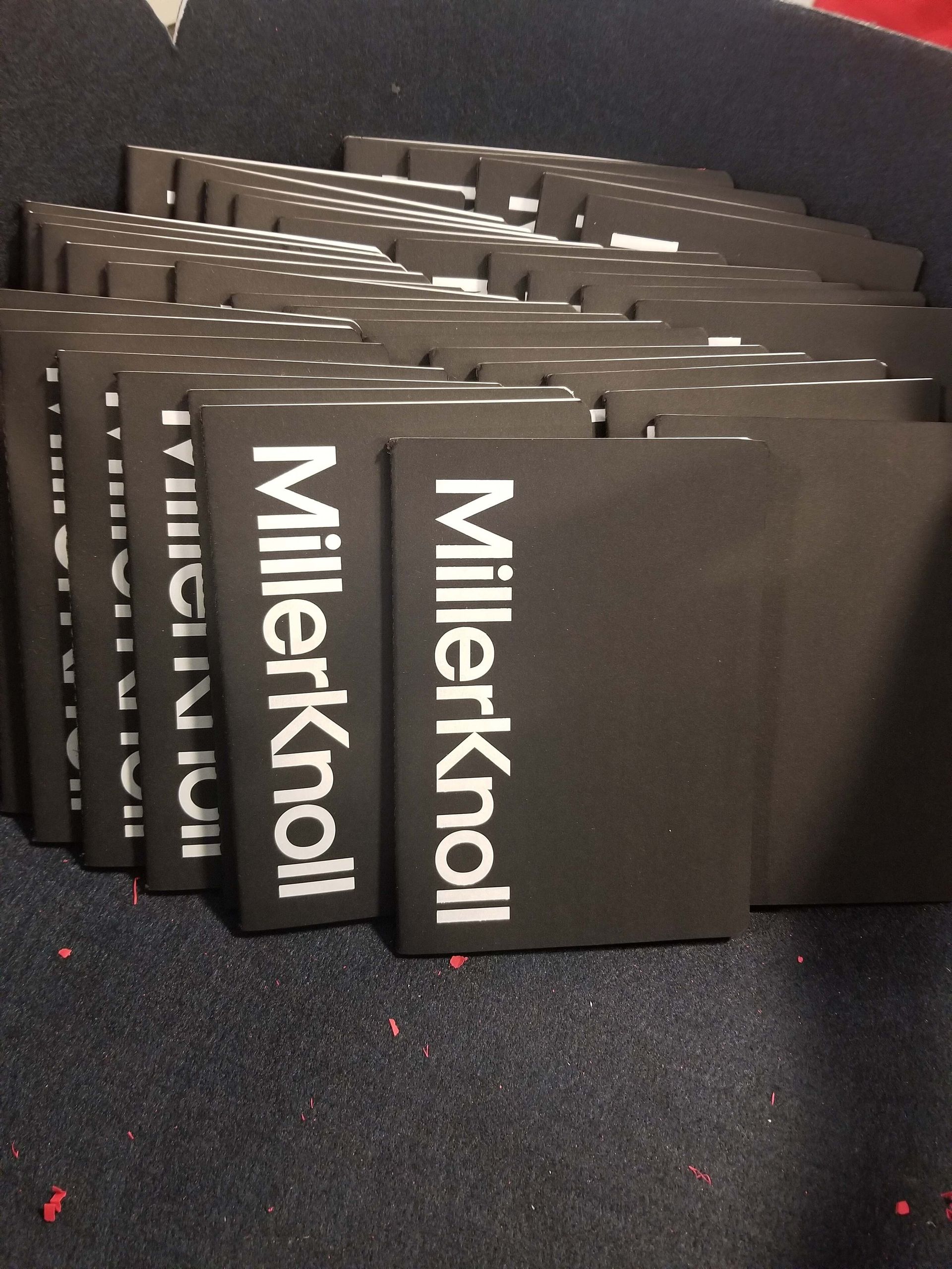 Stacked black Millekroll notebooks on a dark carpet.