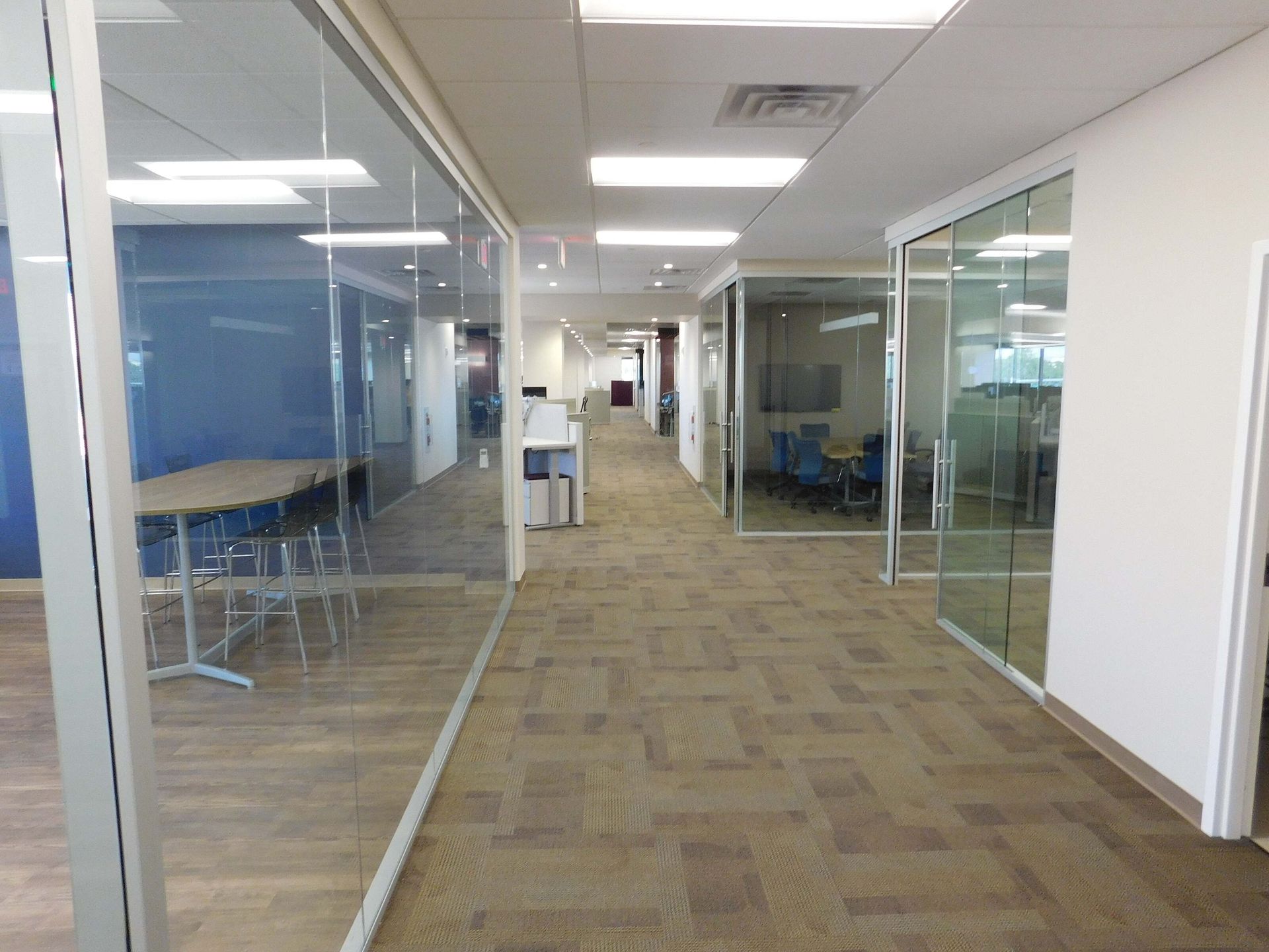 Empty office hallway with glass-walled rooms and carpeted floor