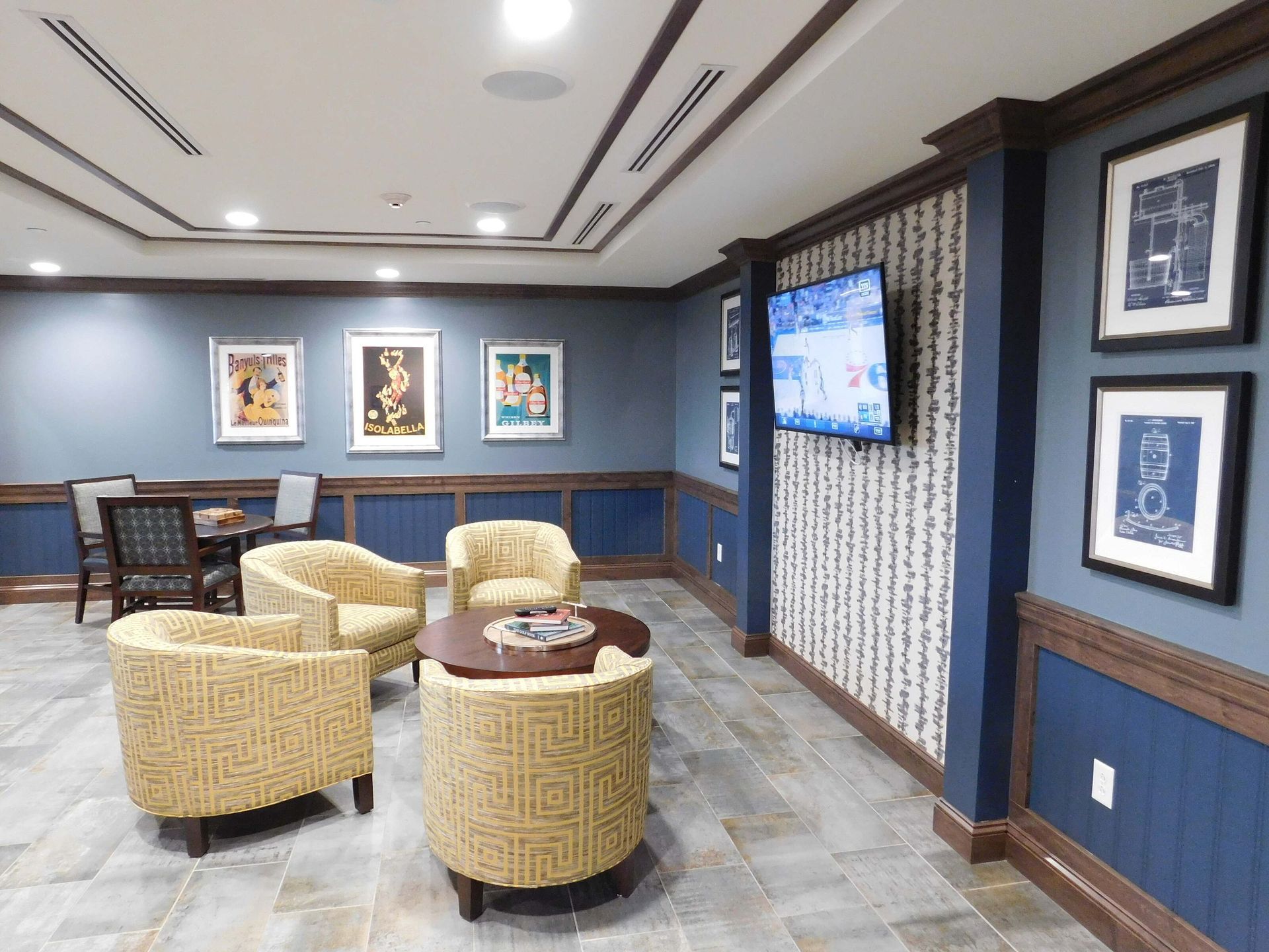 Lounge with wicker chairs and a round table, blue walls, framed art, and a wall-mounted TV.