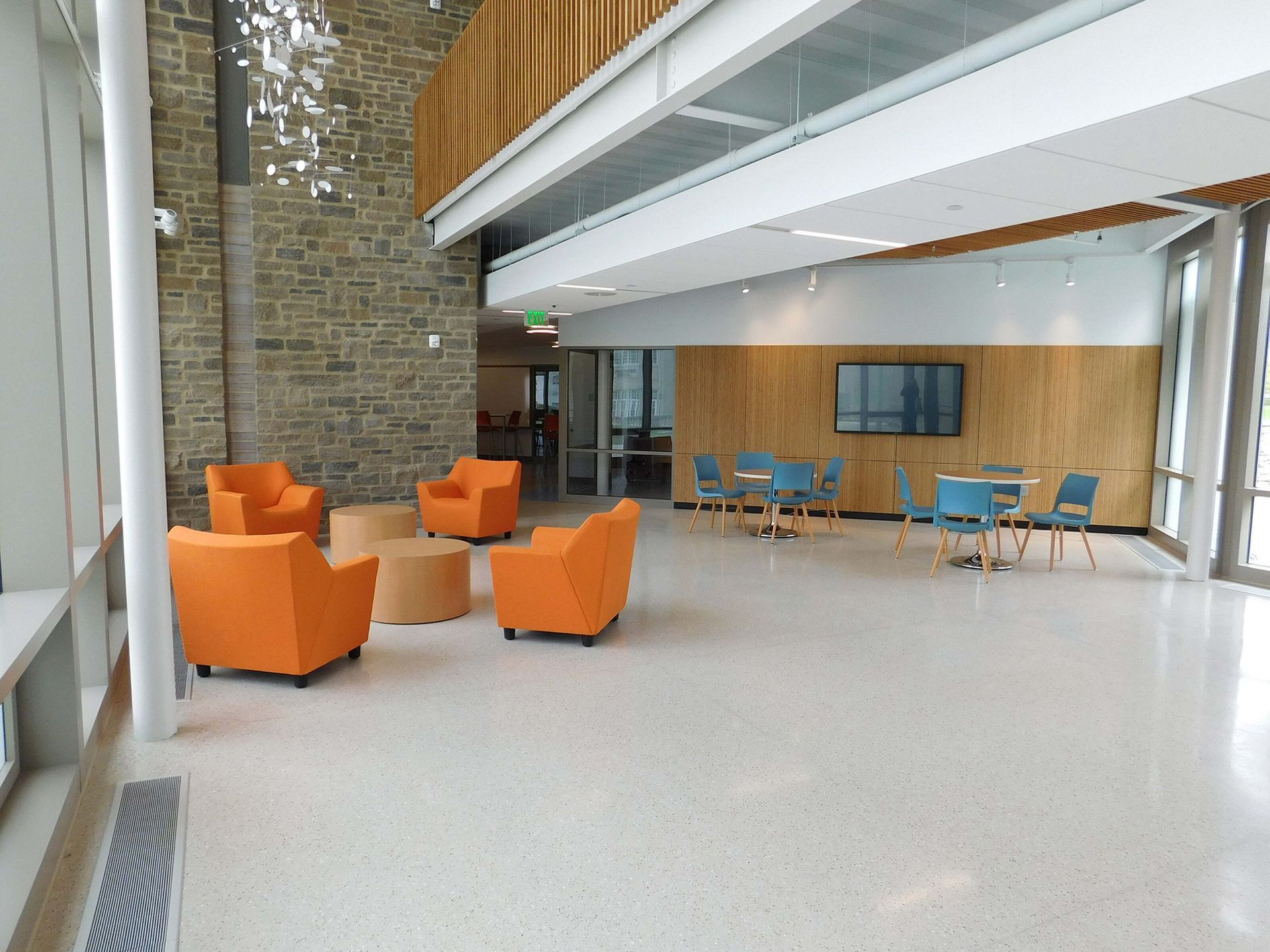 Modern lobby with orange armchairs, blue tables, and a high glass-and-wood interior.