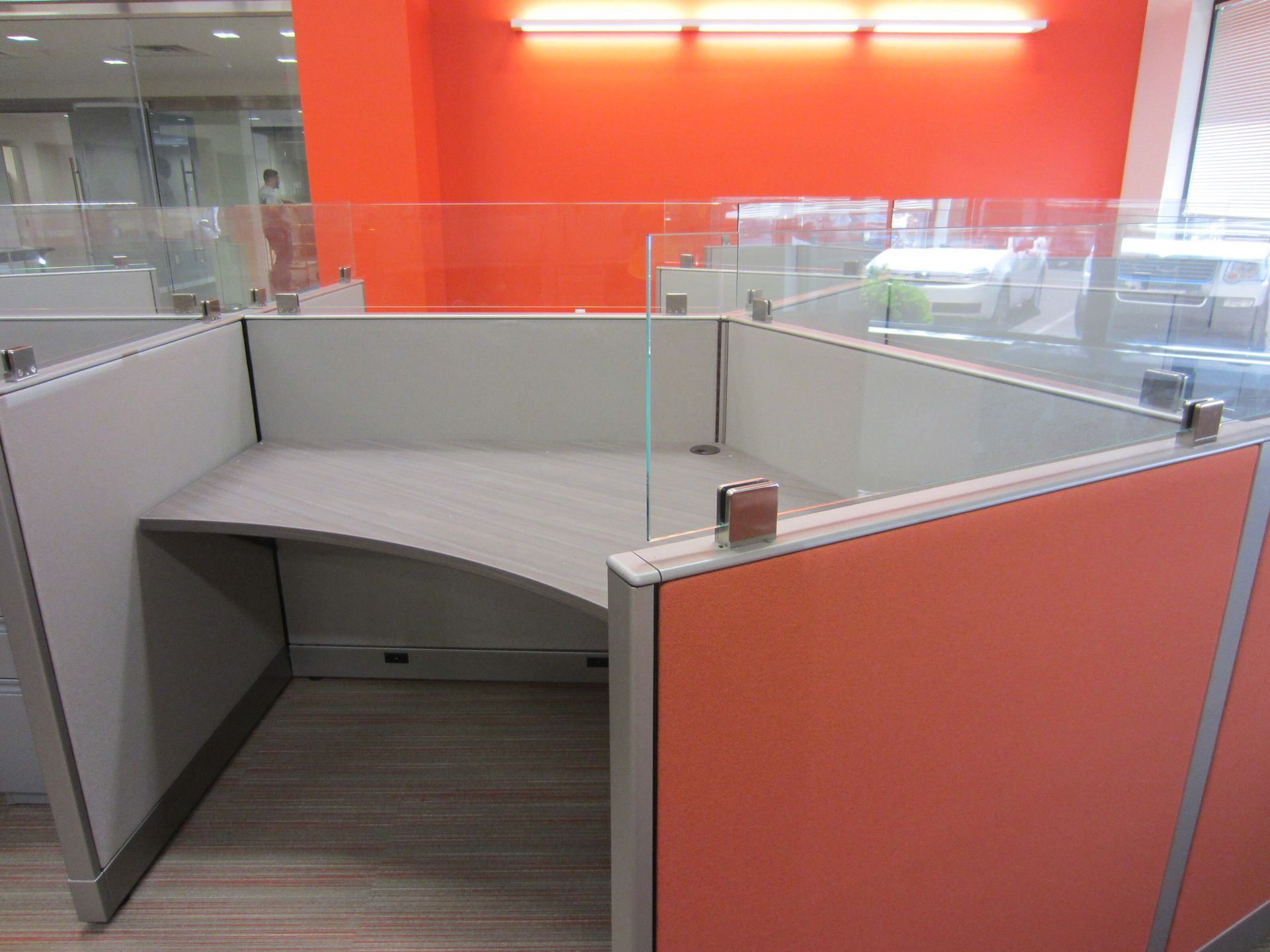 Orange and gray office cubicle with a curved desk and clear partitions