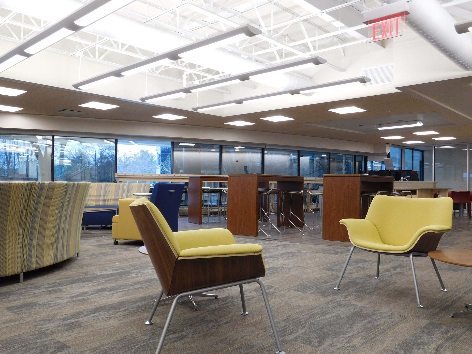 Modern lounge with yellow chairs, carpet, large windows, and ceiling lights.