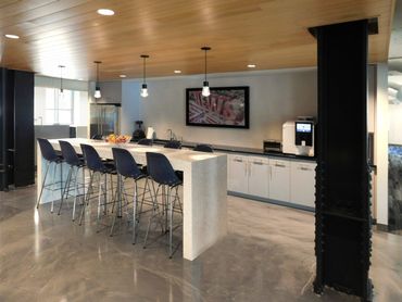 Modern office break room with bar seating, white cabinets, and a wall-mounted TV