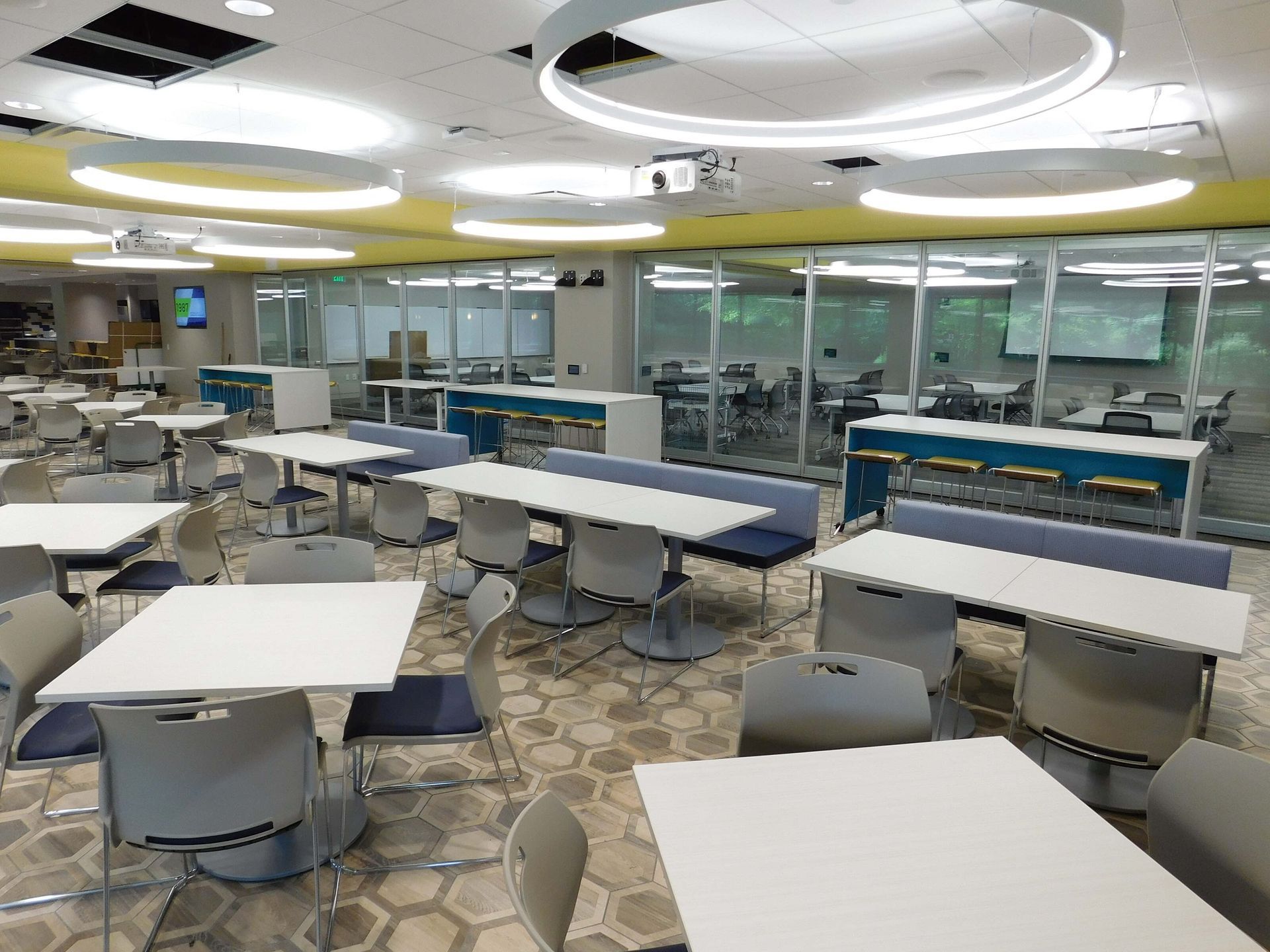 Empty modern cafeteria with white tables, gray chairs, and glass walls under bright circular ceiling lights