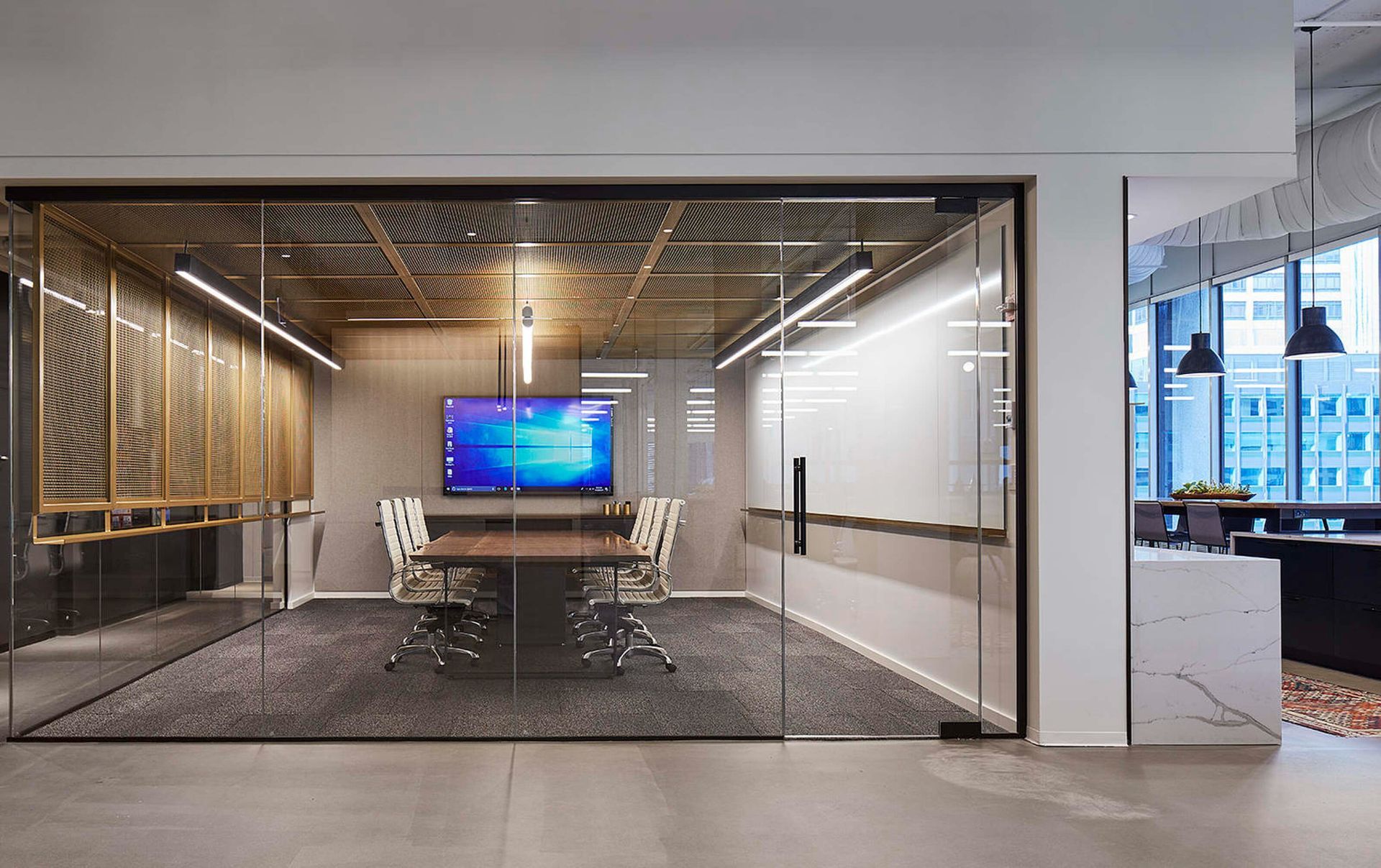 Modern glass-walled conference room with a large screen, long table, and chairs in a bright office.