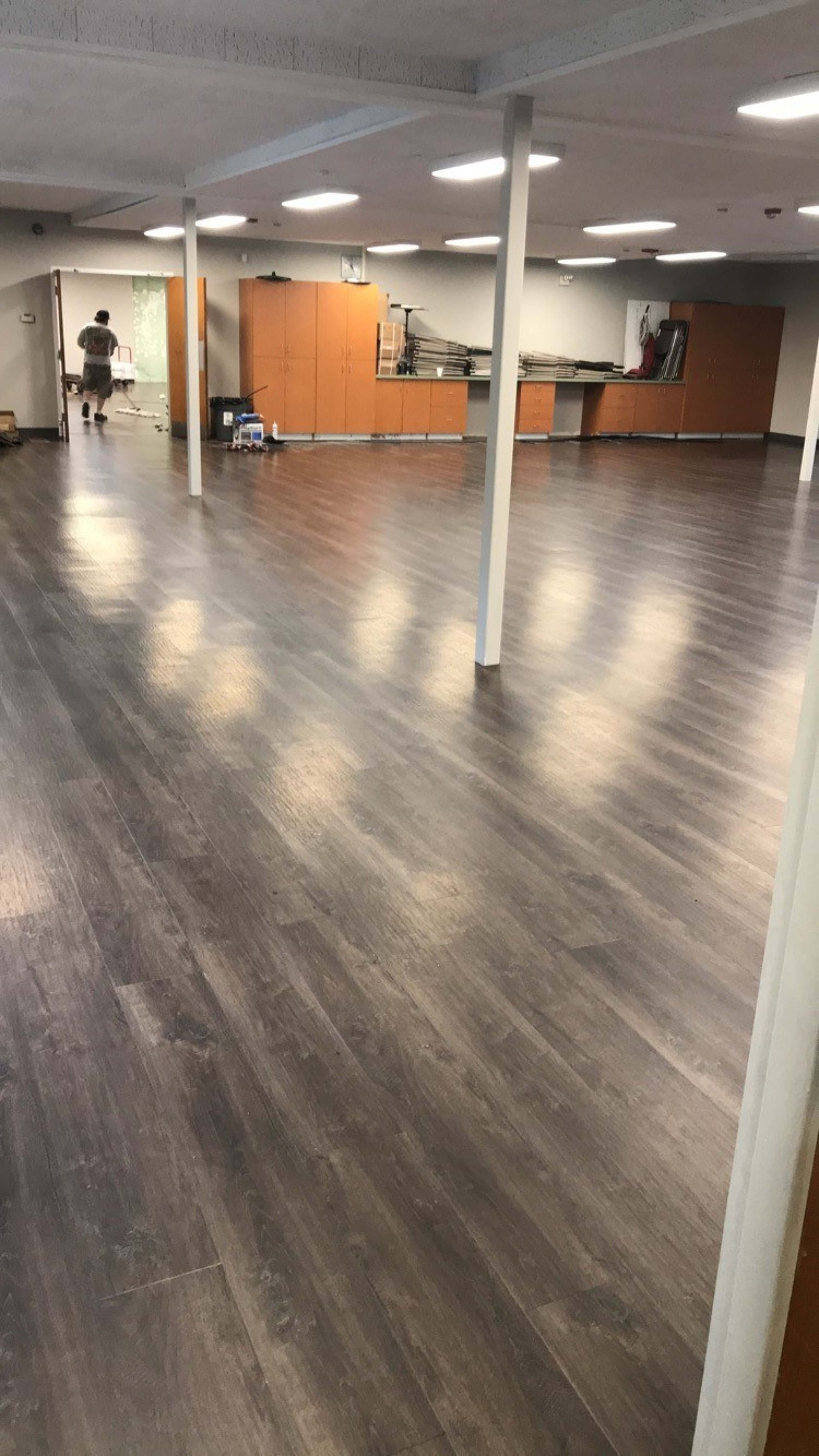 Empty indoor office space with wood-look floors, white columns, and a reception desk in back.