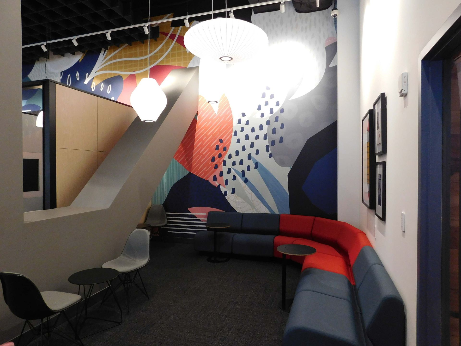 Modern lounge with colorful geometric mural, hanging lights, and curved gray-red seating