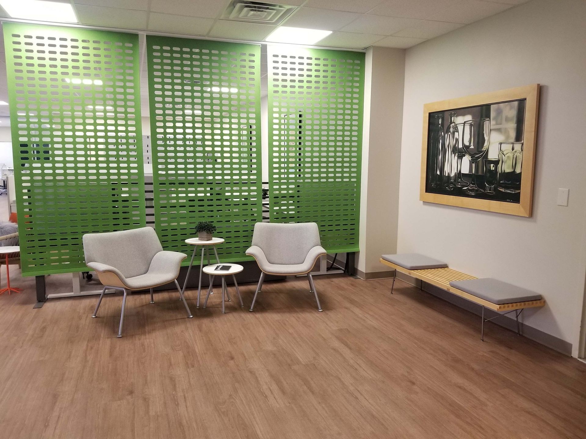 Modern waiting area with white chairs, small tables, green wall panels, and a framed artwork on the wall