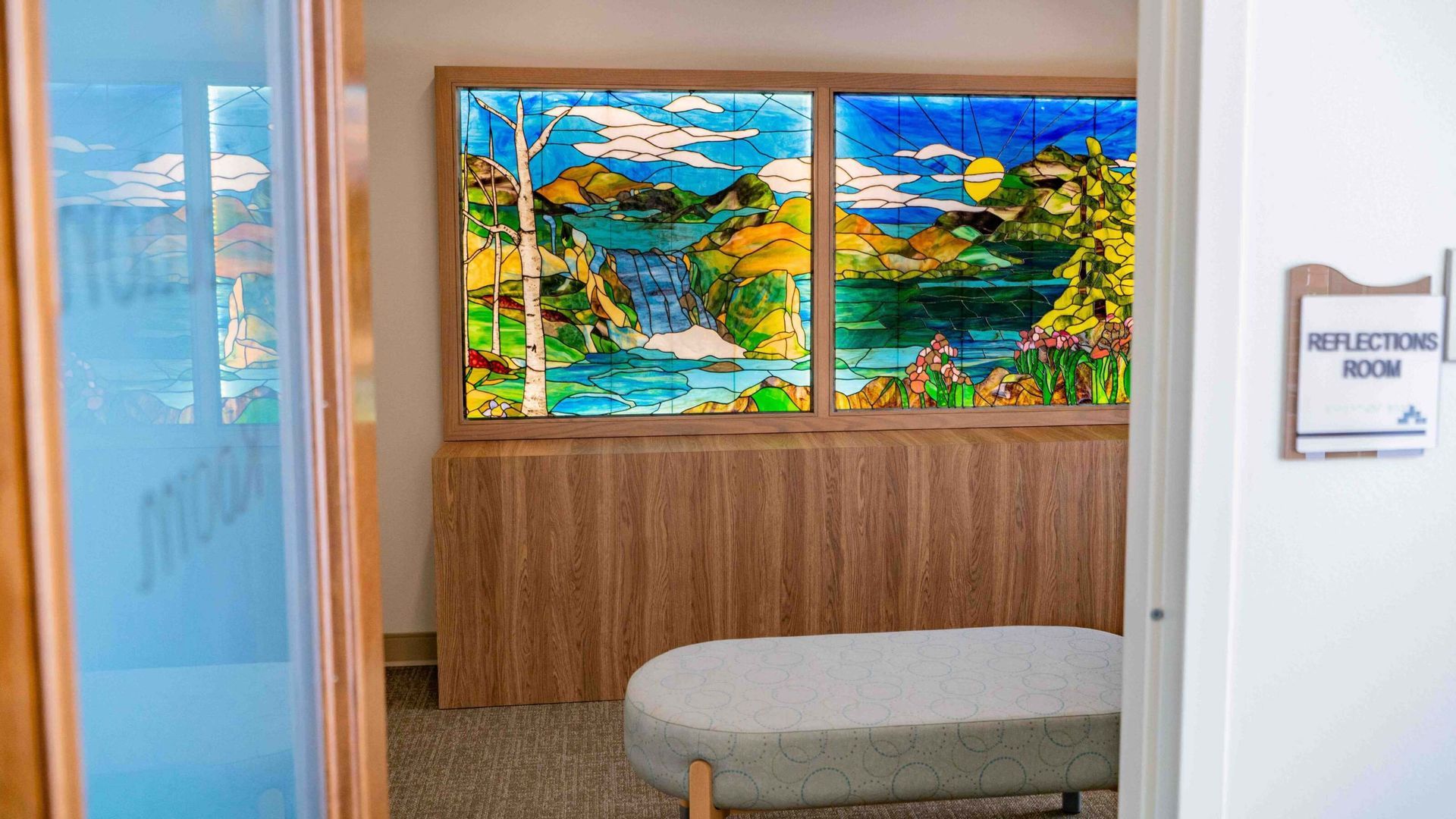 Hospital waiting area with colorful wall art, wooden cabinet, and a bench by a door labeled “Neurology Room.”