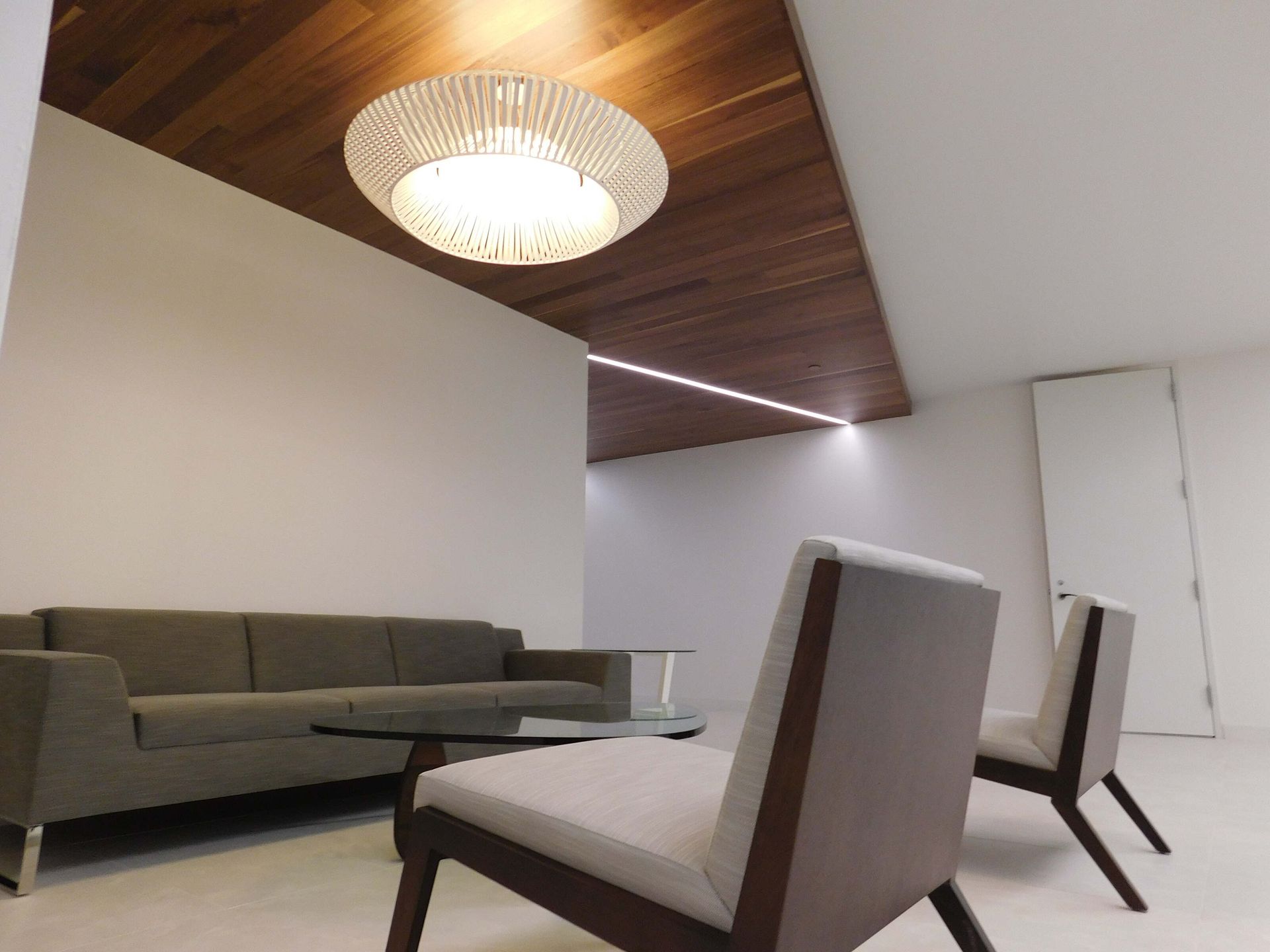Modern living room with gray sofa, white chairs, wood ceiling, and pendant light
